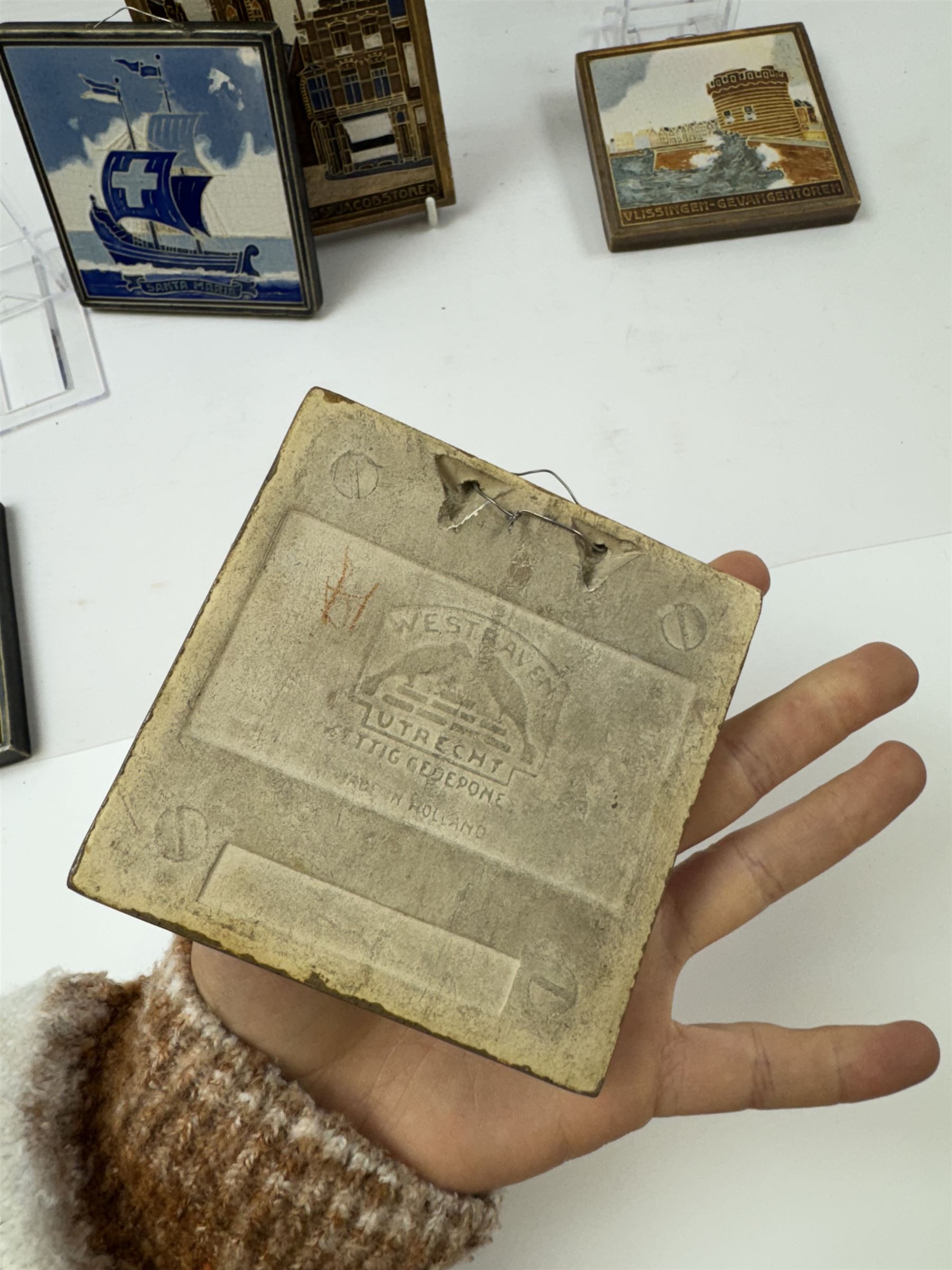 Five Dutch Westraven tiles, to include four square examples depicting maritime and similar scenes, and a rectangular example depicting a village scene, square tiles 10cm x 10cm, rectangular tile 15cm x 10cm