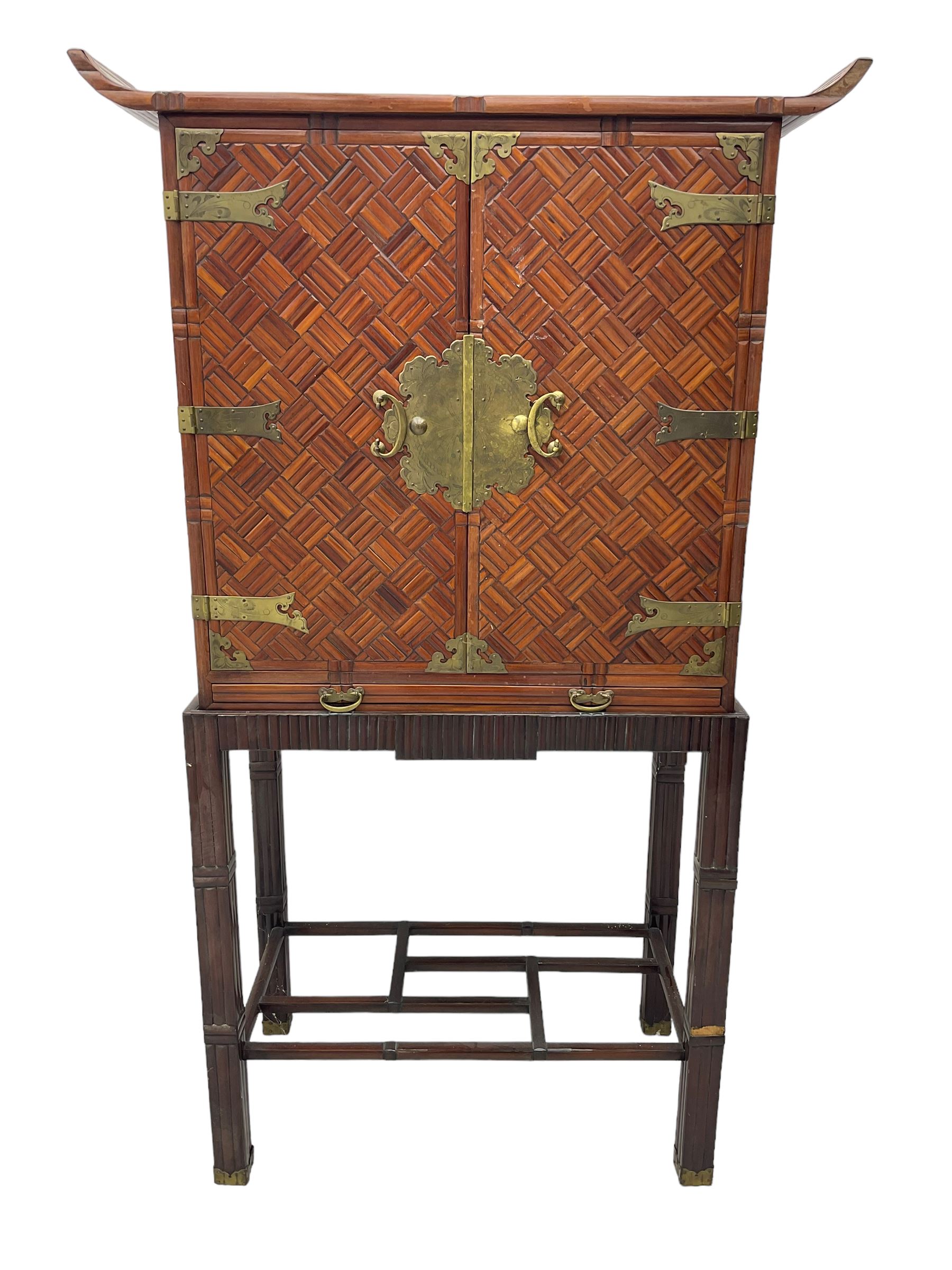 Chinese design bamboo and wood altar cabinet on stand, parquetry lattice-work bamboo, two doors with engraved metal fixtures enclosing drawers and shelf, fitted with slide, the stand pm square supports joined by a series of geometric stretchers