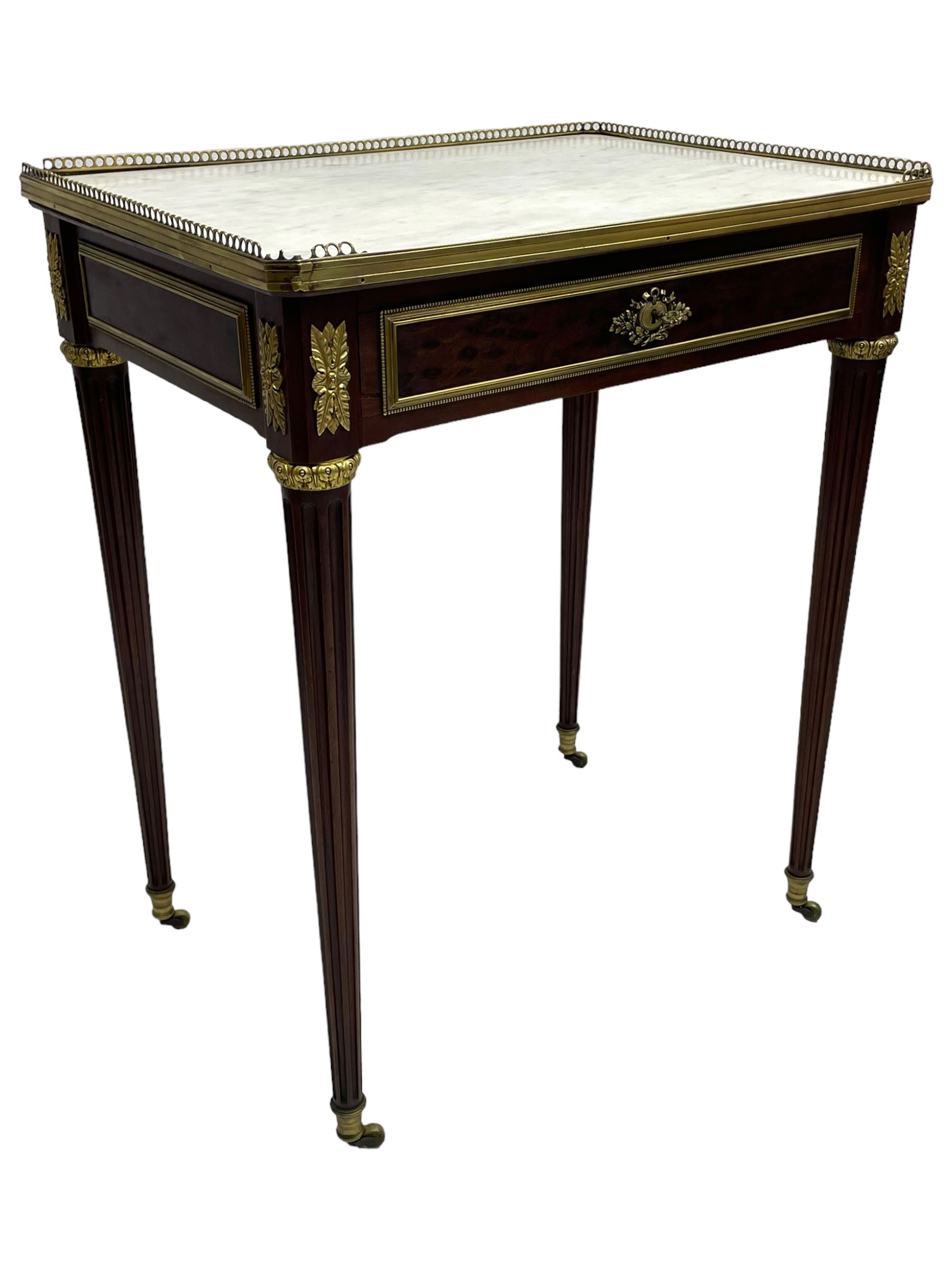 Late 19th century French figured plum pudding mahogany side table, canted rectangular white marble top with raised gilt metal gallery, fitted with a single frieze drawer, central extending floral cast ormolu escutcheon and applied moulded edging, on tapering turned and fluted supports with brass cups and castors, decorated with cast foliate mounts and foliate cast collars 