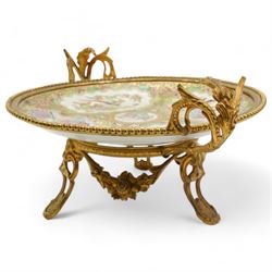 19th century Chinese Canton famille rose circular dish, painted with figures and exotic birds in shaped panels, against a floral and scroll ground, mounted in ormolu style gilt metal twin handled mount with beaded border and three scroll feet, W30cm x H14cm