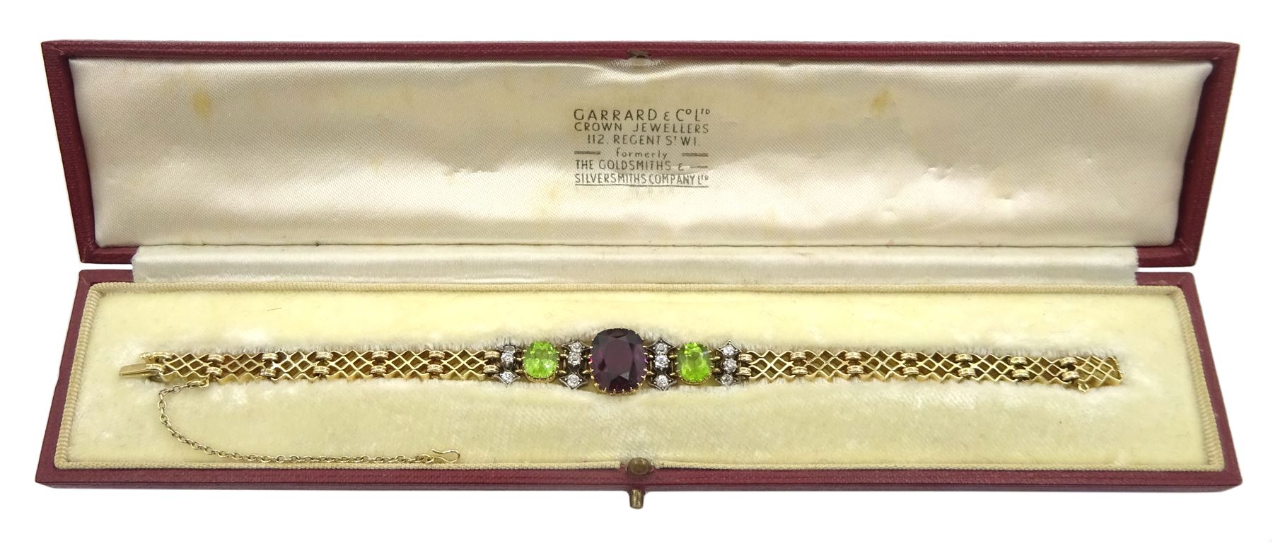 Early 20th century 15ct gold garnet, peridot and diamond, fancy link chain bracelet, the central cushion cut rhodolite garnet of approx 5.05 carat, with two cushion cut peridots set either side, spaced by three old cut diamonds, total diamond weight approx 0.35 carat, in fitted case by Garrard & Co