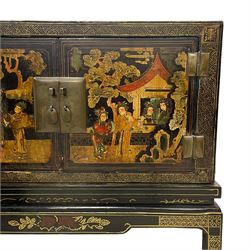 Pair of early 20th century Chinese ebonised and lacquered wood cabinets, the top decorated with dragons over lapping waves within a gilt patterned panel, the surrounding band decorated with Chinese symbols and flowerheads, enclosed by two doors each with village scenes with pagodas, figures and trees, the panelled sides decorated with a figure riding a dragon on stands with gilt decorated 