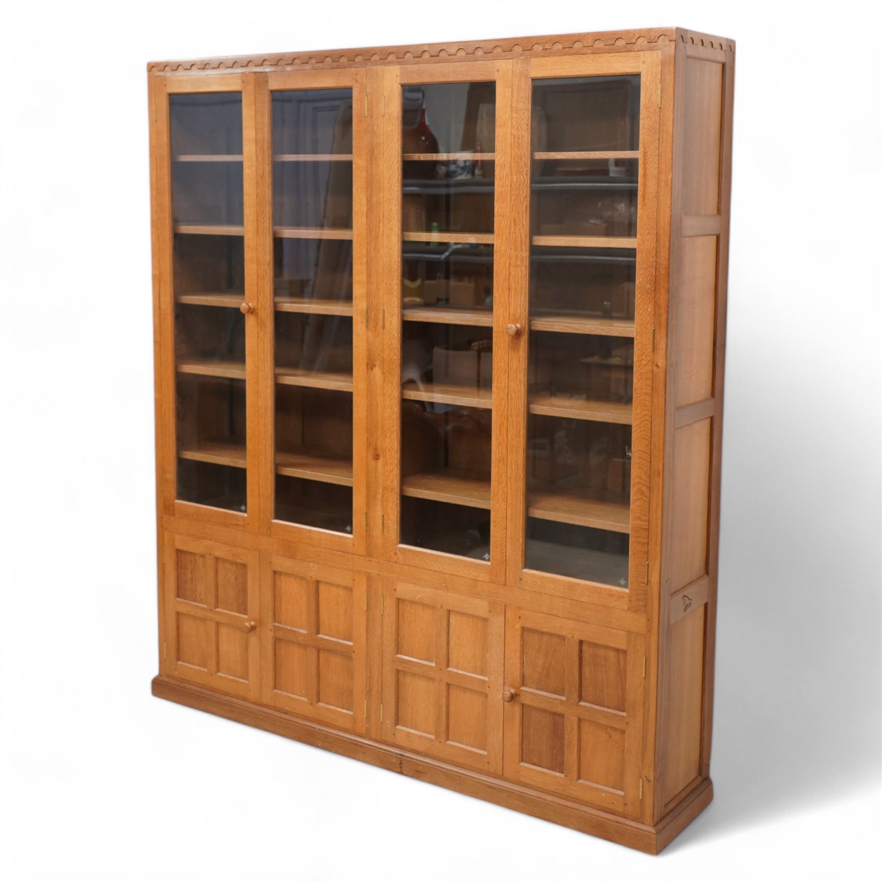 Eagleman - oak bookcase, penny moulded cresting rail over four glazed doors and four panelled doors, fitted with adjustable shelves, on moulded plinth base, panelled sides, carved with eagle signature, by Albert Jeffray, Sessay, Thirsk