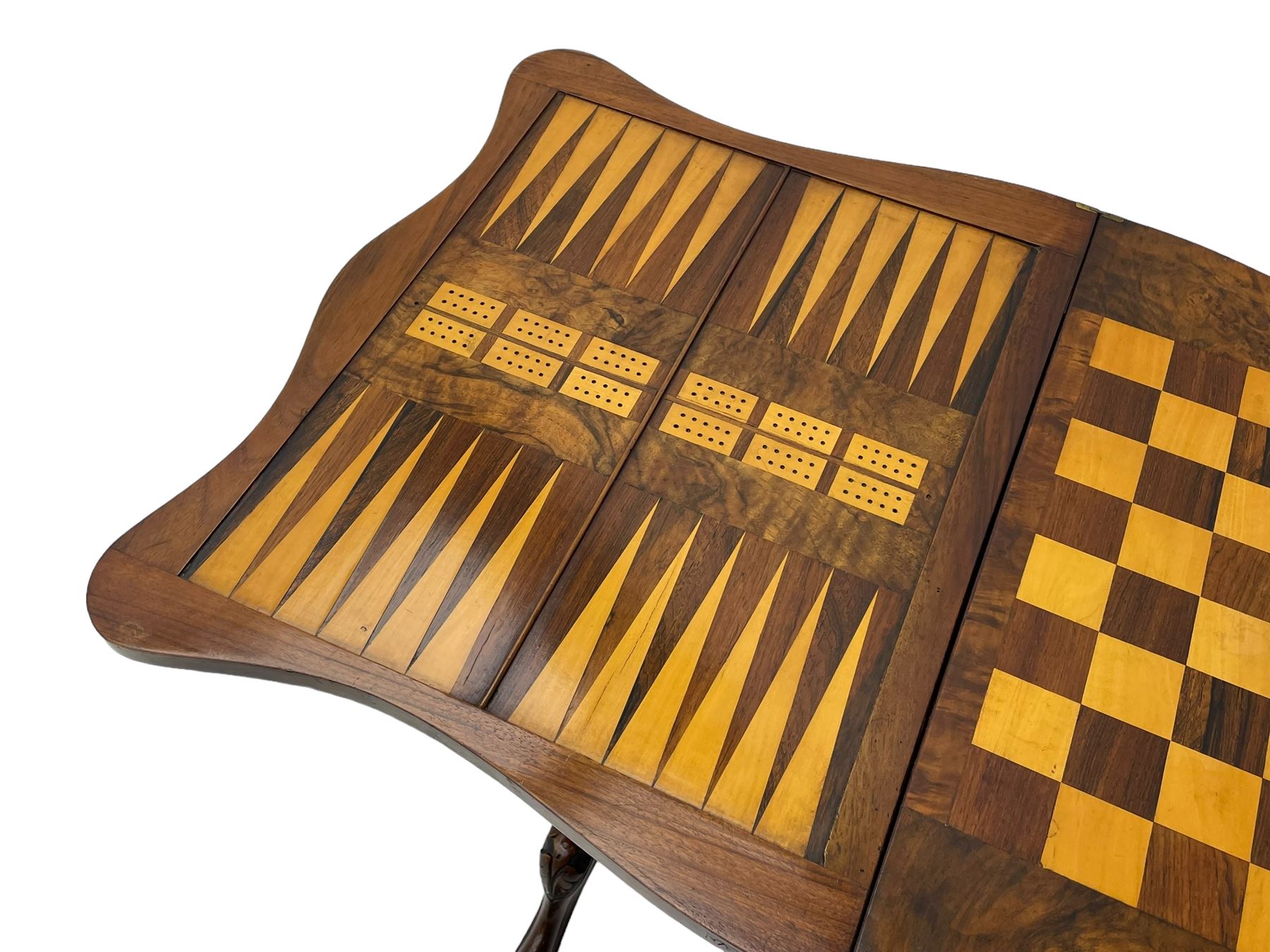 Victorian inlaid figured walnut games table, the serpentine fold-over top inlaid with scrolling foliate decoration, the top opens to reveal cribbage, backgammon and chess boards, single drawer over sliding storage well, on twin pillar supports united by double turned stretchers, on foliage carved out-splayed supports with brass and ceramic castors 