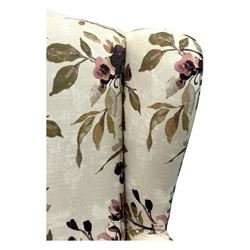 Hardwood-framed wingback armchair, upholstered in cream floral pattern fabric, on turned front feet