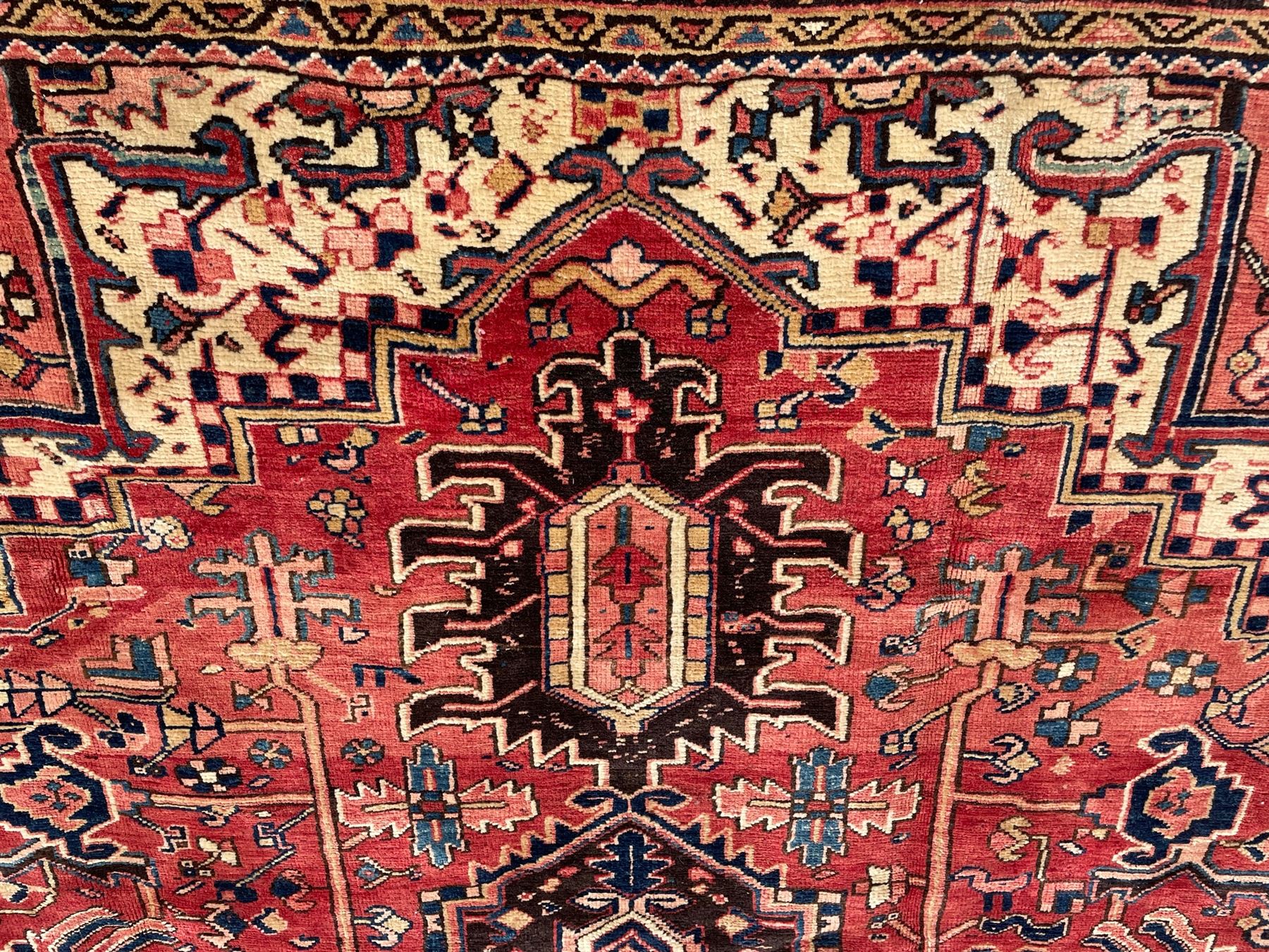 Persian Heriz red ground carpet, large central eight point medallion with projecting palmettes surrounded by small geometric motifs, decorated profusely with hooks, rosettes and animals, the busy border decorated with stylised foliate motifs within guard stripes 