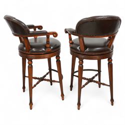 Pair of hardwood-framed bar stools, revolving tub seat with buttoned back rest and upholstered seat in brown leather, reed moulded seat rail over four lobe carved tapering supports, united by metal foot rest and x-framed stretchers 