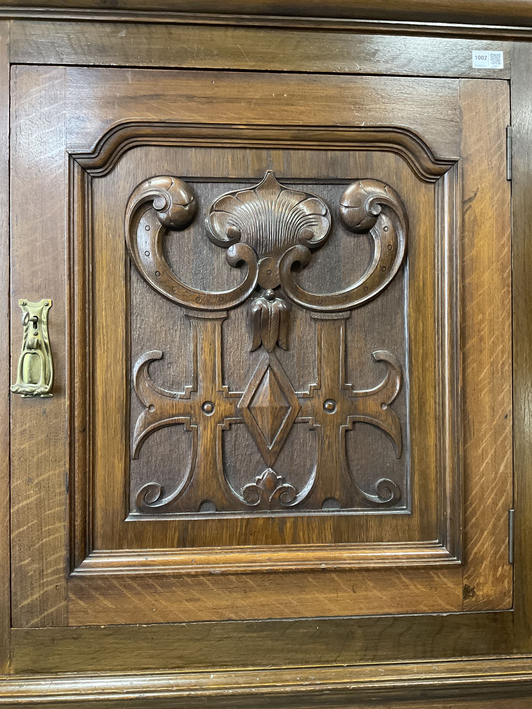 Arts & Crafts period oak corner cabinet, projecting cornice over astragal glazed door and single panelled door decorated with applied carved foliate scrolls and stylised roods surrounded by moulded edge, enclosing single shelf