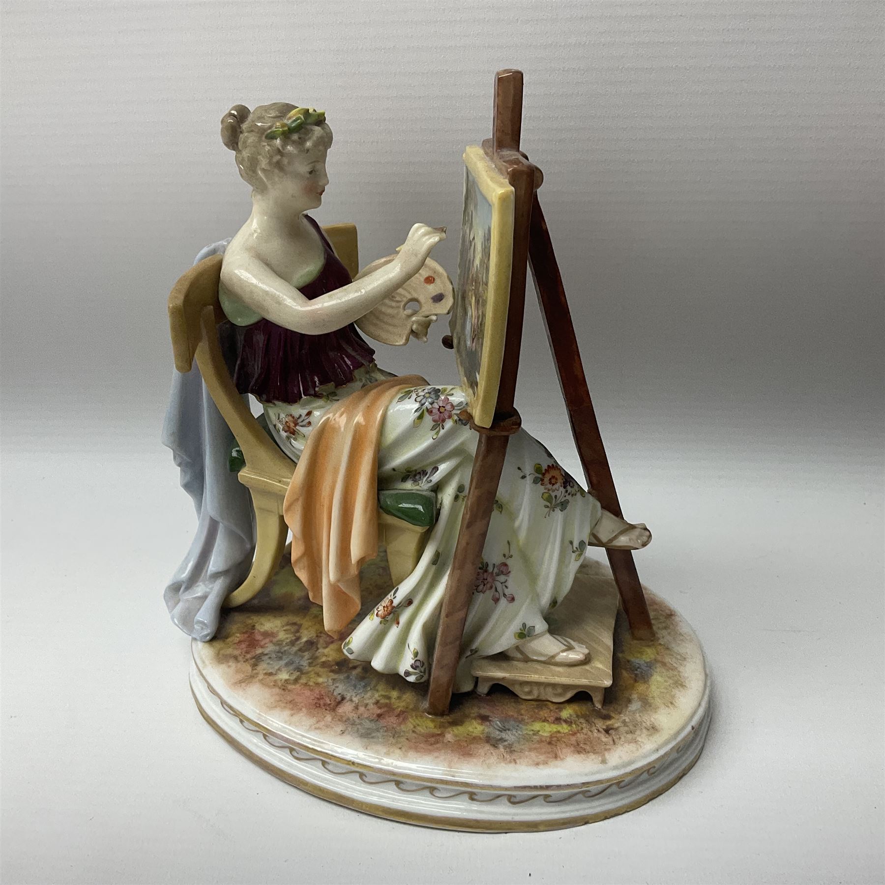 Pair of late 19th/early 20th century Naples figures modelled engaged in the arts, the first example modelled as a female figure seated before an easel, painting a figural scene, the second modelled as a female figure seated before a bust with scultping tools in hand, each upon an oval base with naturalistic painted ground, each with blue crowned N mark beneath, each approximately H16cm, including base L15xm
