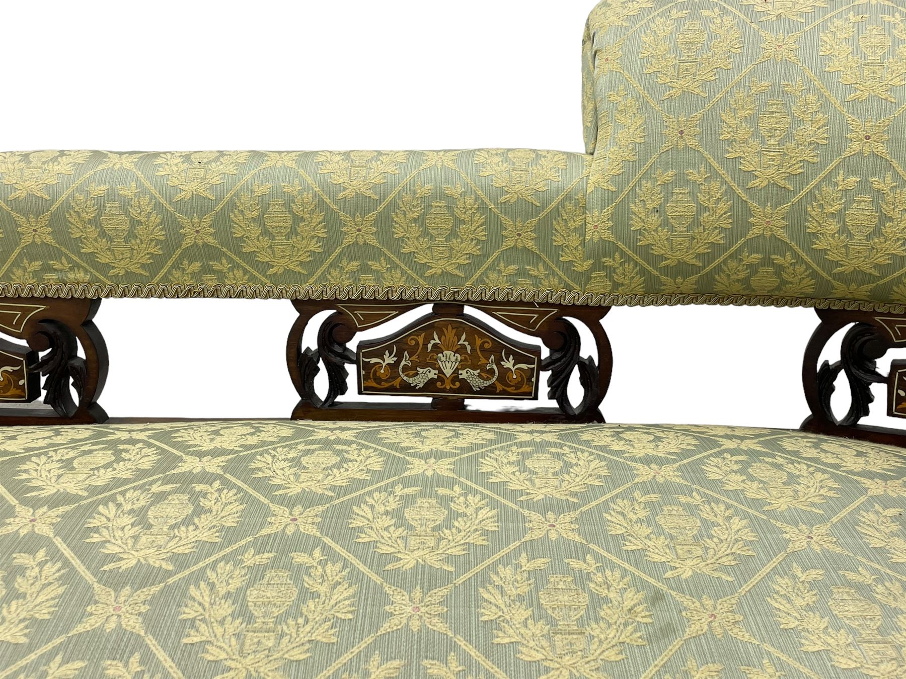 Late Victorian walnut salon settee or chaise lounge, double-ended with rolled back and curved end, upholstered in light aquamarine fabric with raised repeating lozenge pattern, decorated with laurel leaf wreaths and urns, three pierced splats carved with curled leaves, inlaid with dolphins and scrolled foliate motifs in simulated ivory and boxwood, on tapering ring turned supports with brass and ceramic castors (L166, D60, H70cm); together with matching tub-shaped armchair (W61cm, H73cm, D66cm)  