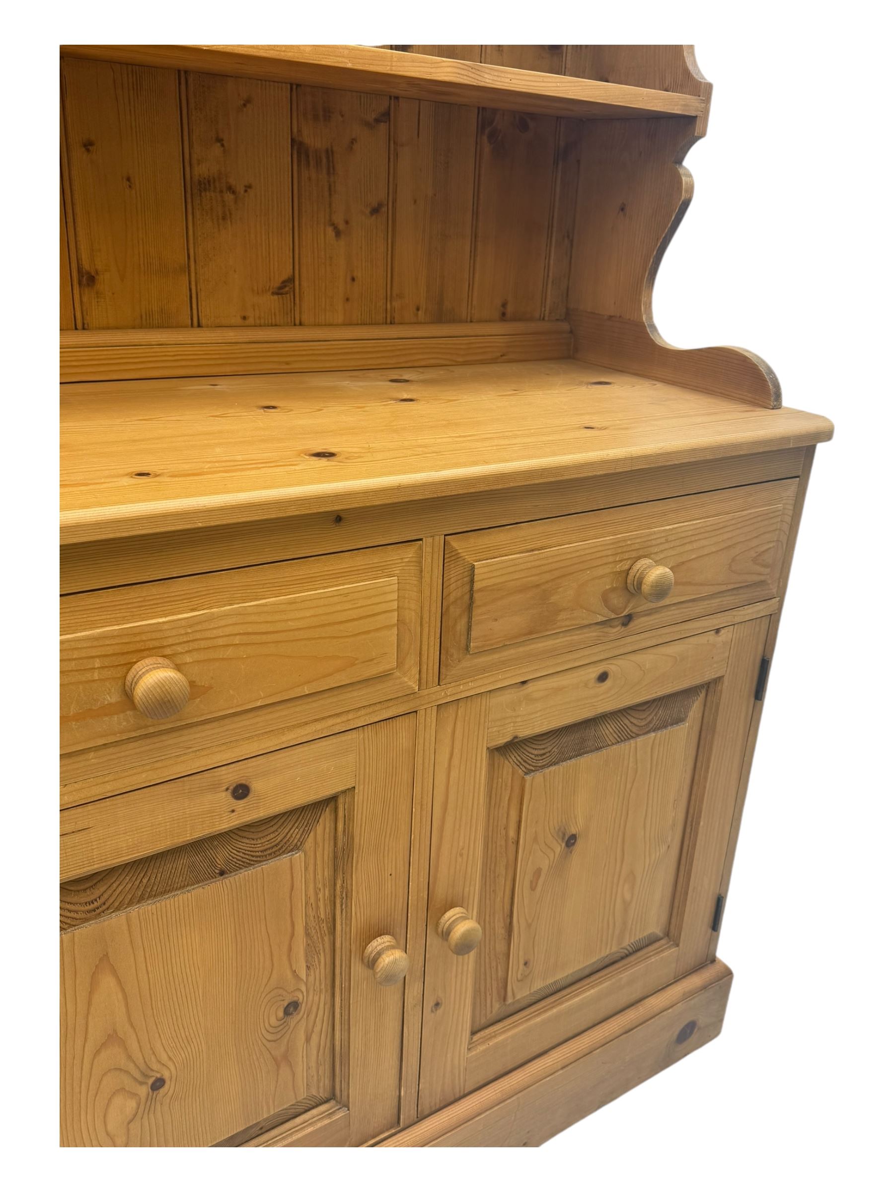 Large traditional pine dresser, shaped cornice over three open shelves, base fitted with four drawers above four panelled cupboards, each with turned wooden knobs, on plinth base