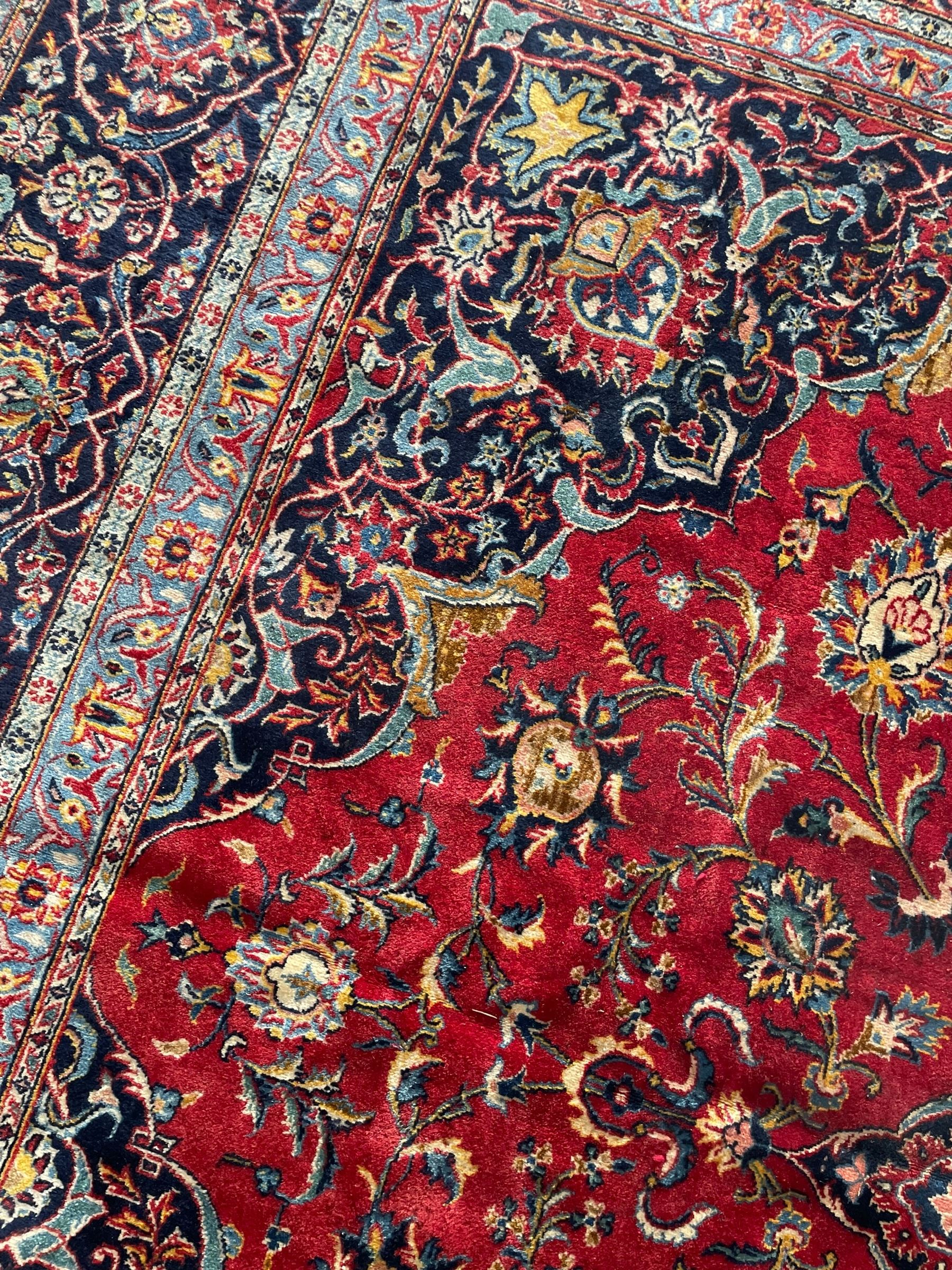 Persian Kashan crimson ground carpet, central rosette medallion on a field of trailing foliate branches decorated with palmettes, scrolling border with repeating plant motifs and flower heads, enclosed within floral pattern guard stripes