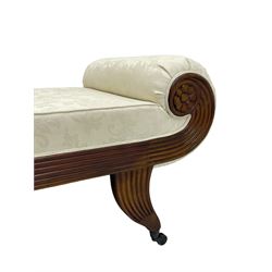 Regency design mahogany chaise longue, scrolled arms with carved rosette details, upholstered in cream damask fabric with bolster cushion, reeded frame supported by turned legs on brass castors