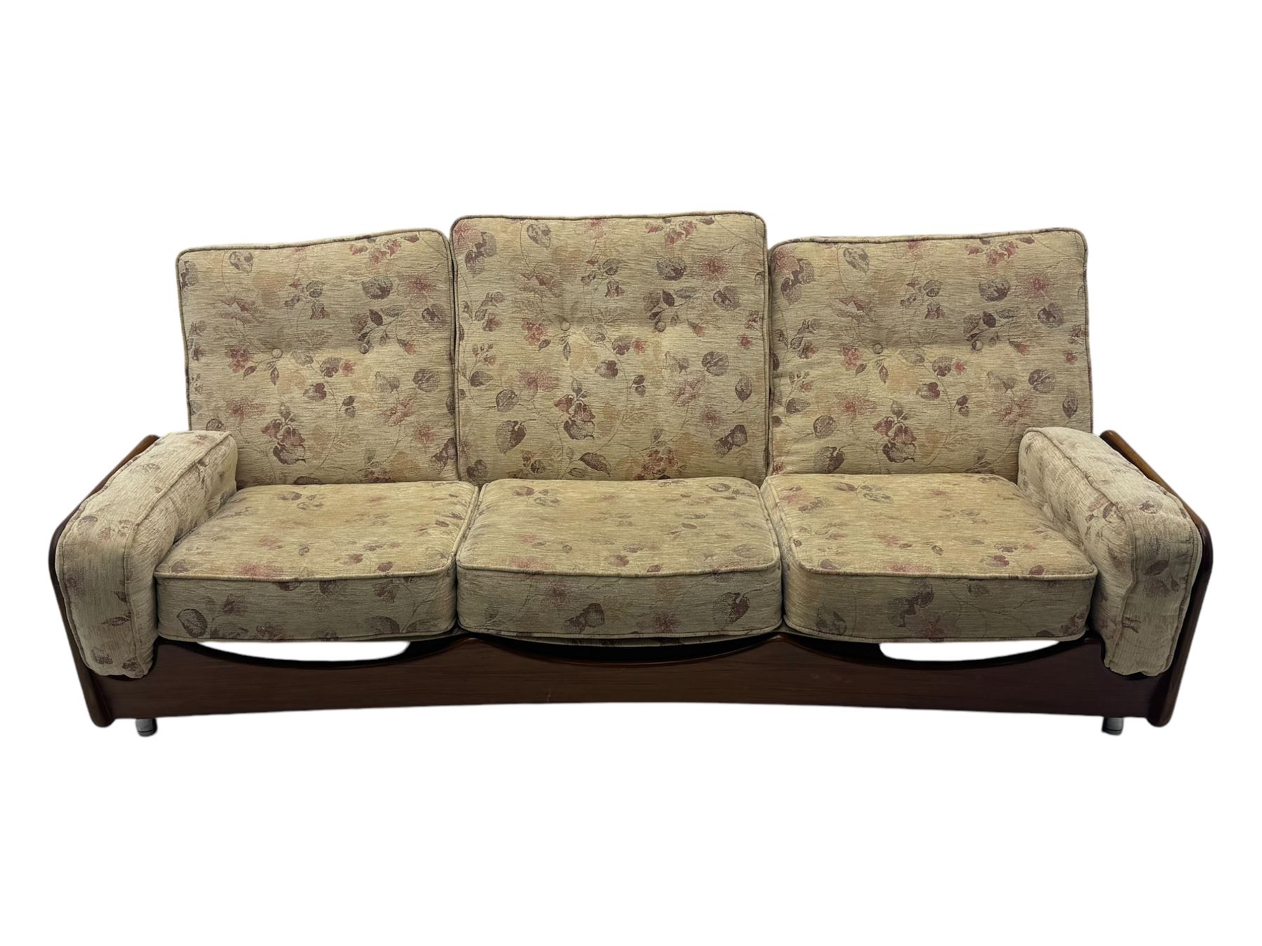 Mid-20th century three-seat sofa with floral patterned upholstery, supported by a sculpted teakwood frame with curved cutout detailing, loose cushioned back and seat, on tubular metal feet