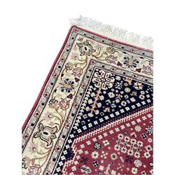 Persian design crimson ground rug, the field decorated with tree of life and floral motifs, enclosed by indigo spandrels with stylised flower head decoration, repeating scrolling border 