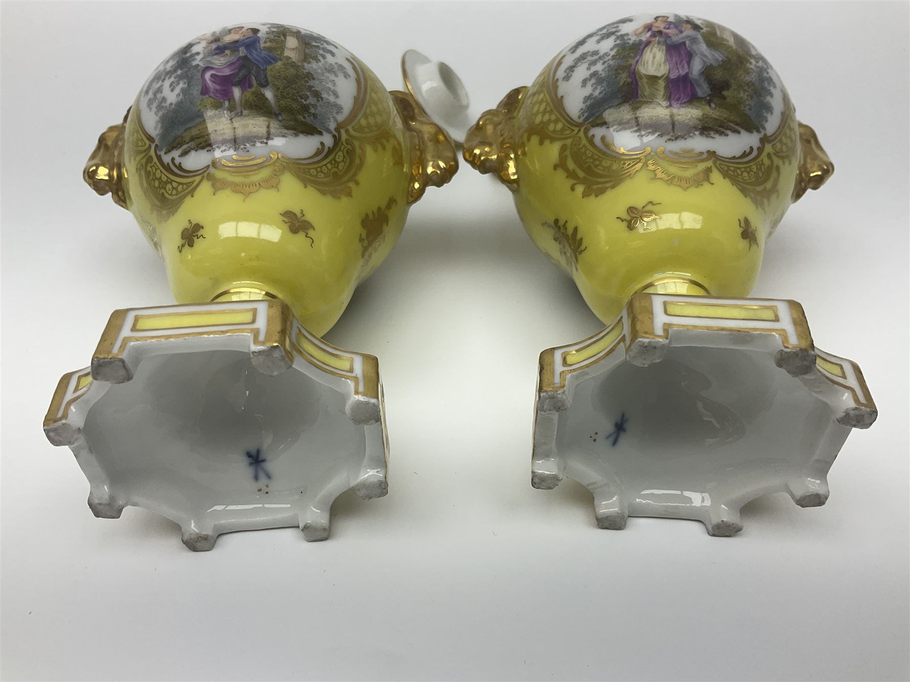 Pair of early 20th century Dresden vases with cover, of baluster form, decorated with figural panels within ornate gilt borders upon a yellow ground, with twin gilt goat mask handles, H16.5cm