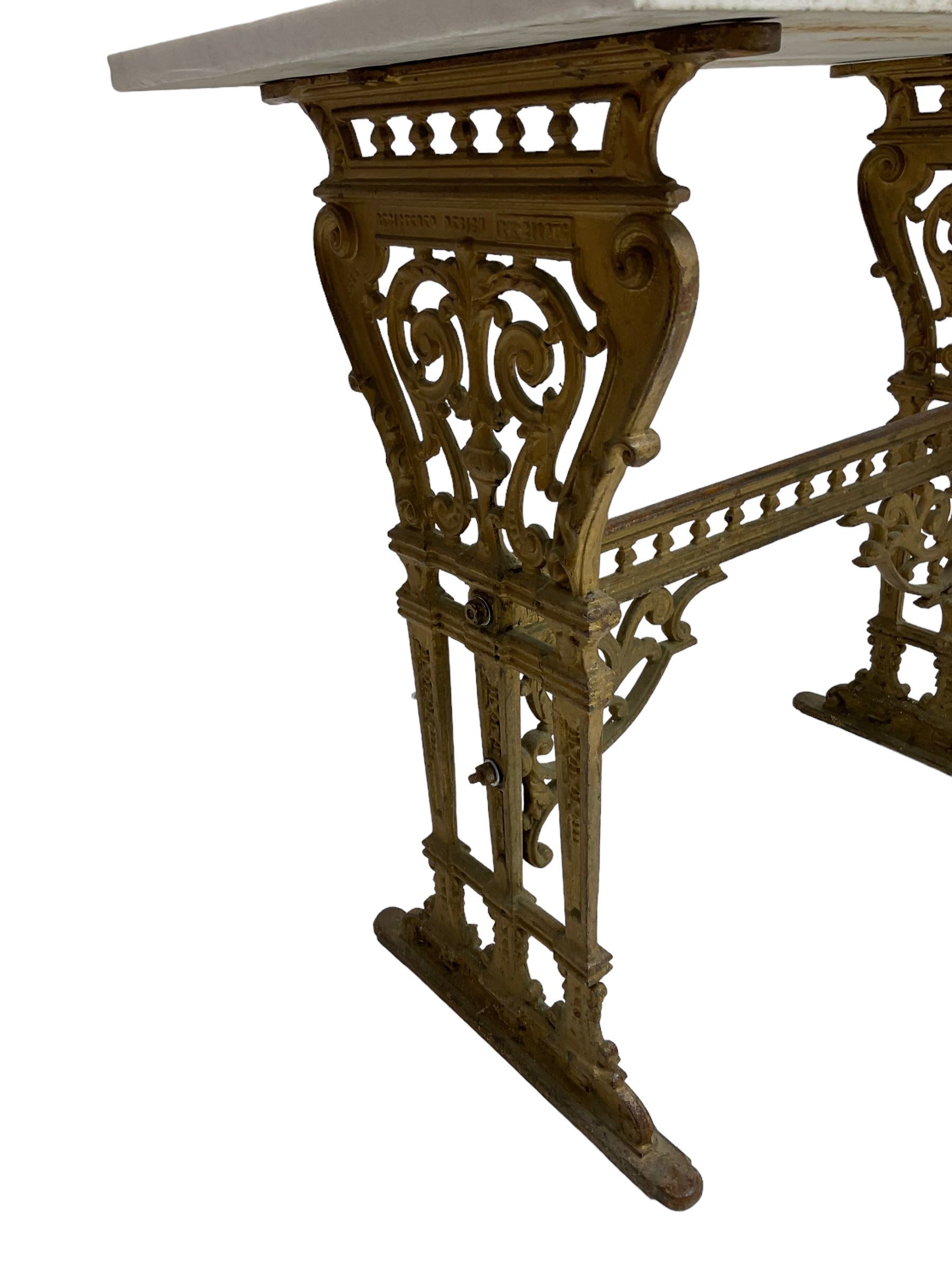 Pair of 19th century cast iron entrance tables, rectangular marble top over ornate gilt bases with scrolling foliate design and sledge feet, united by balustrade stretcher with scroll spandrels