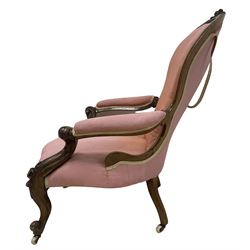 Victorian mahogany framed open armchair, spoon-back and sprung seat upholstered in pink fabric, scrolled arm terminals over serpentine fronted seat decorated with moulded carved floral motifs, cabriole supports with ceramic castors