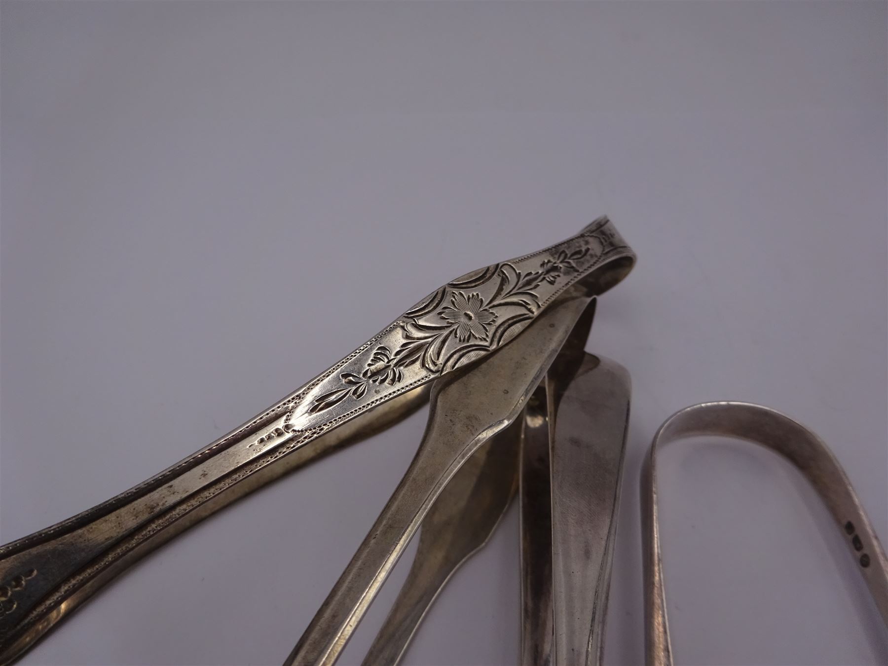 Four pairs of silver sugar tongs, to include three George III pairs comprising a bright cut engraved example, hallmarked Peter, Ann & William Bateman, London 1801, a fiddle pattern example, with engraved initials, hallmarked Thomas Wallis II, London 1806 and one other, hallmarked Stephen Adams II, London 1800, together with an Edwardian pair, with shell bowls, hallmarked Mappin & Webb Ltd, Sheffield 1909