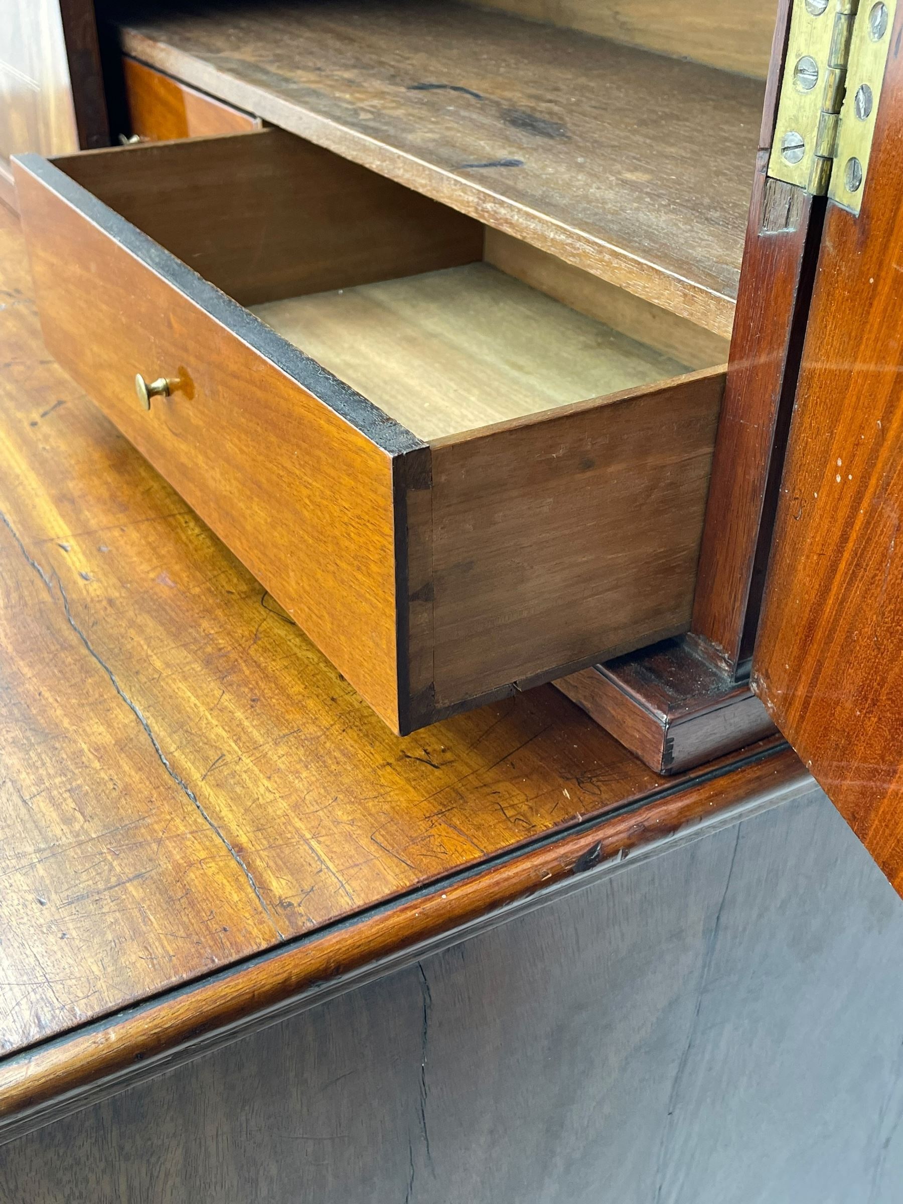 George III figured mahogany secretaire bookcase, projecting moulded dentil cornice decorated with single row of roundels, two figured mahogany doors with boxwood and ebony stringing enclosing three adjustable shelves and three drawers, moulded rectangular top over four long scratch-moulded drawers, the top secretaire drawer with fall front enclosing small drawers, pigeon holes and inset writing surface, shaped apron with bracket feet