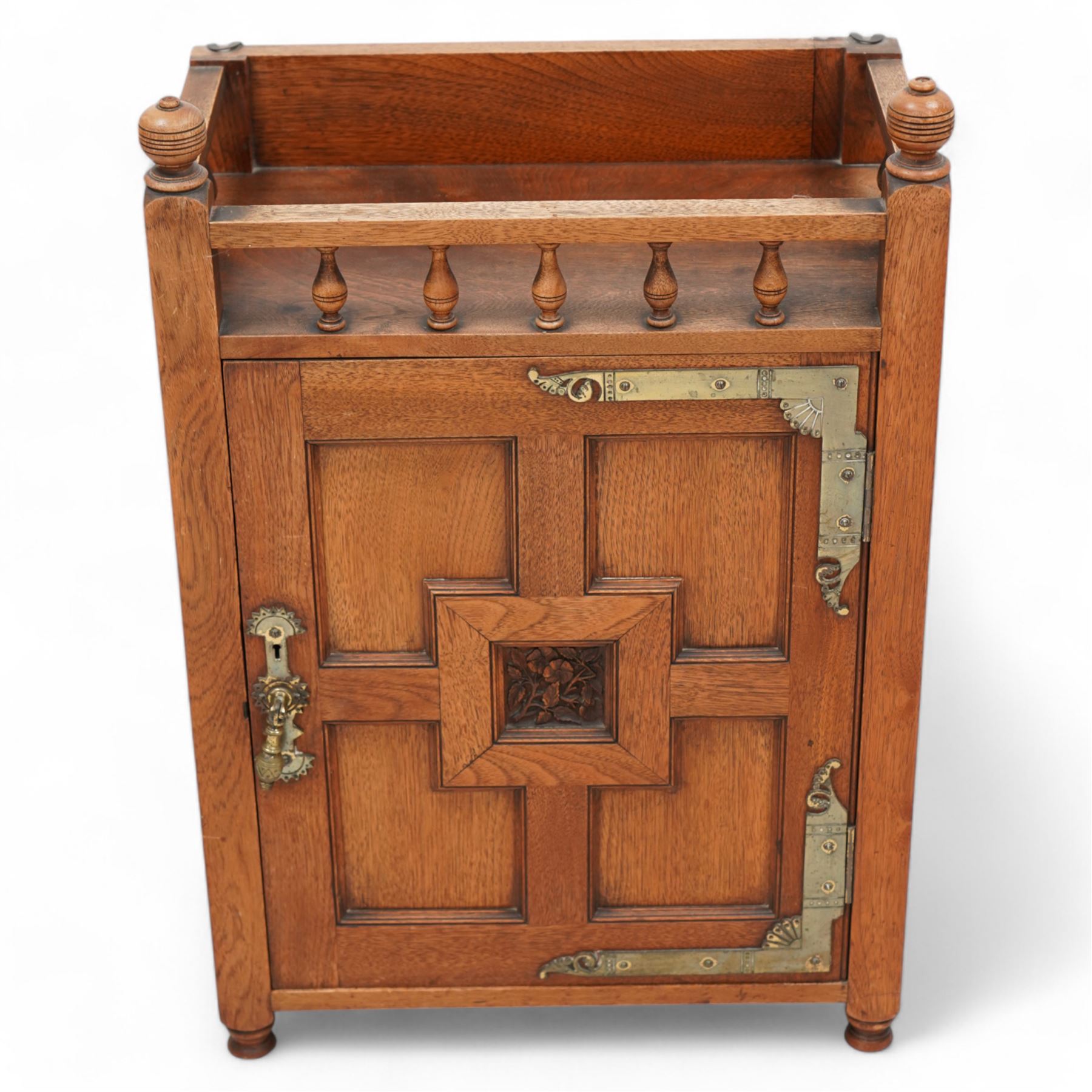 Late 19th century Aesthetic Movement walnut cupboard, raised and pierced spindle gallery surmounted by ring-turned finials, over a panelled door decorated with central foliate carved panel and surrounded by plain geometric shaped panels, applied with brass fittings and loop handle, on turned feet