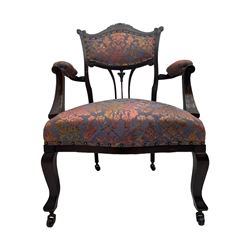 Late Victorian mahogany framed armchair, upholstered in muted purple fabric with iridescent floral pattern and nailhead trim, central foliate carved splat over padded scrolled arms, on cabriole supports fitted with castors