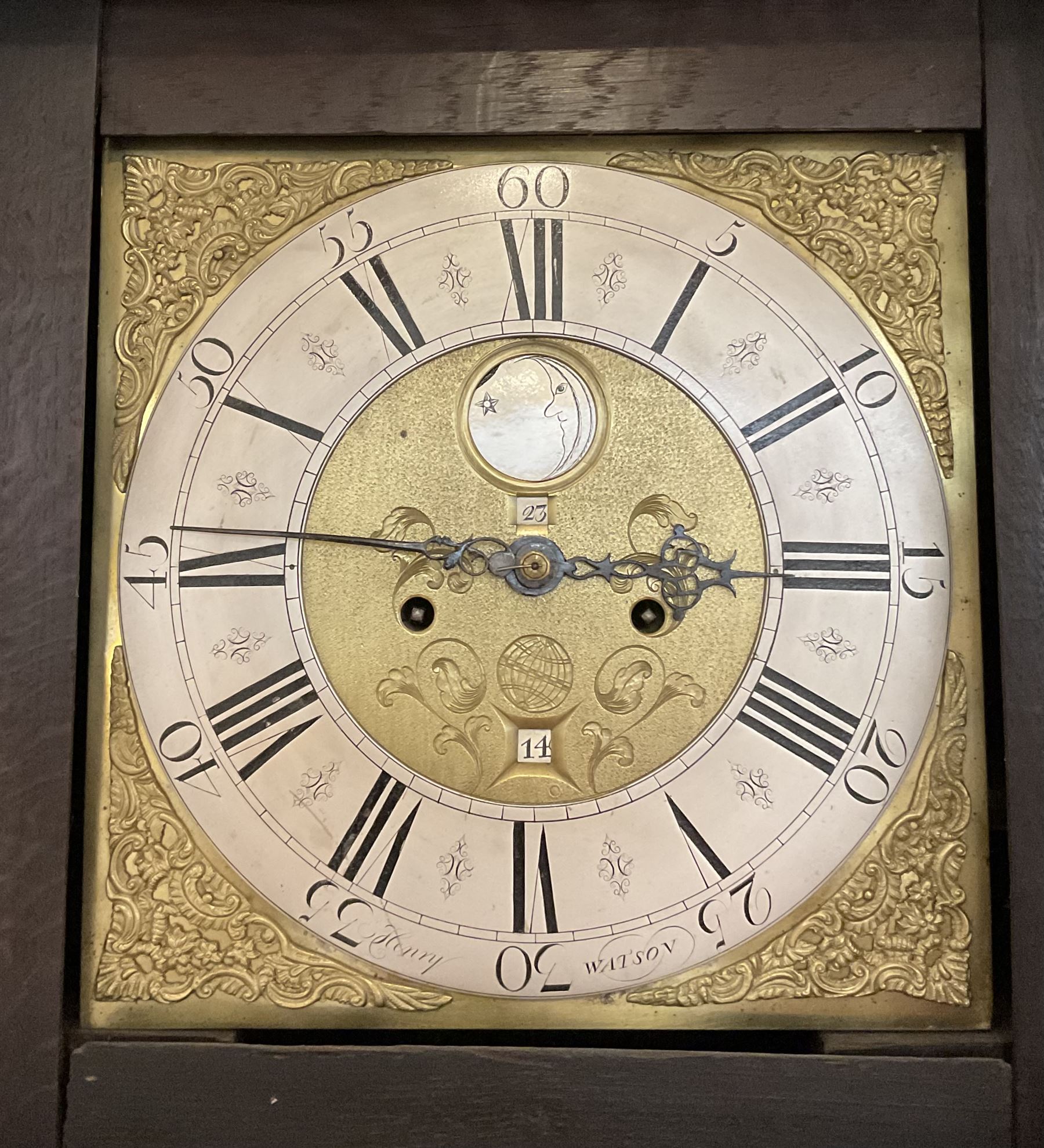 Henry Watson of Huddersfield  - mid-18th century 8-day oak longcase with a flat caddy top and turned pilasters flanking the hood door, trunk with three quarter columns and a long trunk door raised on a rectangular plinth, brass dial with cast spandrels, matted and engraved dial centre, penny moon with lunar and calendar date, silvered chapter ring with Roman numerals, five minute Arabic's, hour and quartet hour tracks, dial pinned directly to an inner countwheel striking movement, sounding the hours on a bell. With weights and pendulum.