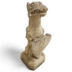 Near pair of cast stone garden seated dragons, snarling jaw holding shield on chamfered base 