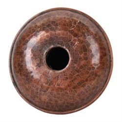 Large Arts & Crafts copper chamberstick, the circular dish with tall cylindrical stem, circular nozzle, and applied strap handle, the whole with hammered finish, with impressed mark beneath, H22cm