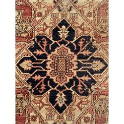 Persian Heriz design rug with red ground, the field featuring a central medallion with floral and geometric motifs, surrounded by ivory spandrels, the main border showcasing a series of floral patterns on a dark blue ground