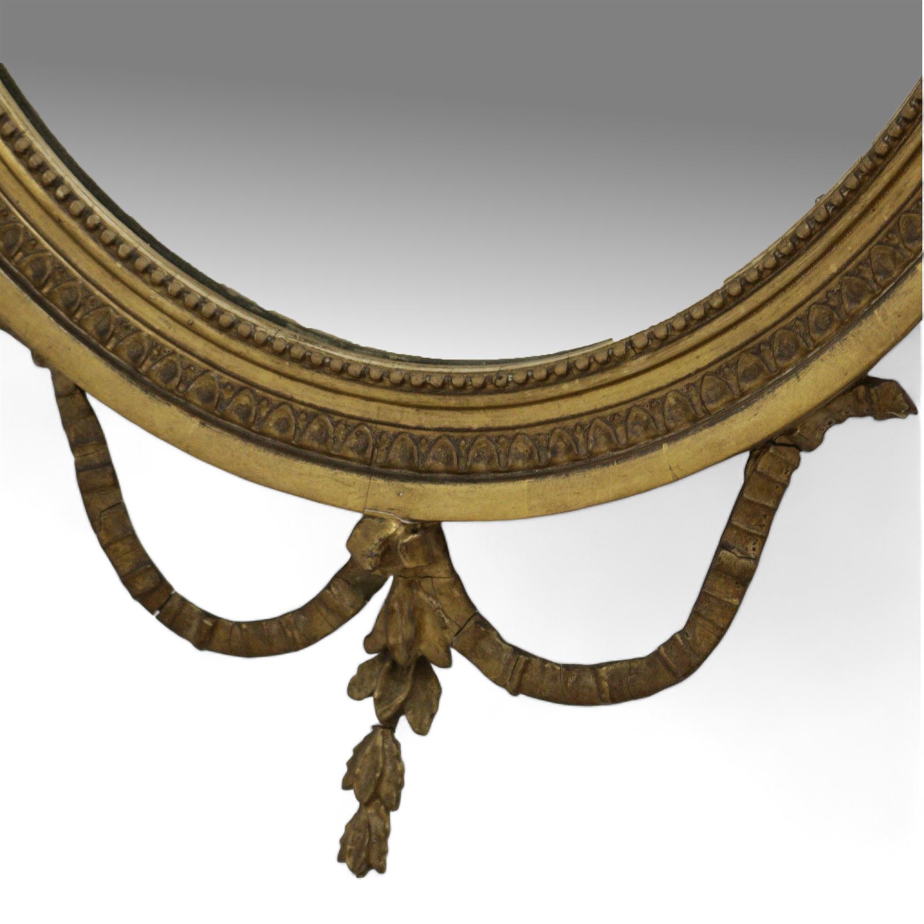 Late 19th century giltwood and gesso wall mirror, oval foliate moulded frame surmounted by urn and bell flower garlands, bevelled mirror plate 