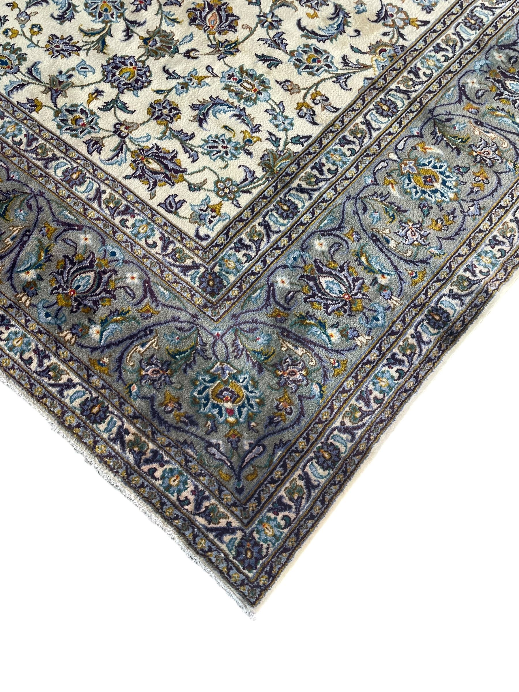 Persian Kashan ivory ground carpet, the busy field decorated with scrolling and interlaced leafy branches and palmettes, trailing branch border with repeating stylised plant motifs, within floral pattern guard stripes 