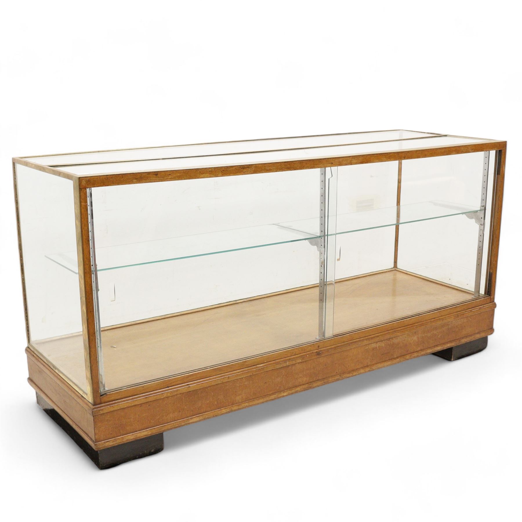 Early 20th century glazed oak and brass bound shop's display cabinet or haberdashery cabinet, fitted with two sliding glass doors, two glass shelves on chromed metal supports, black finish block feet