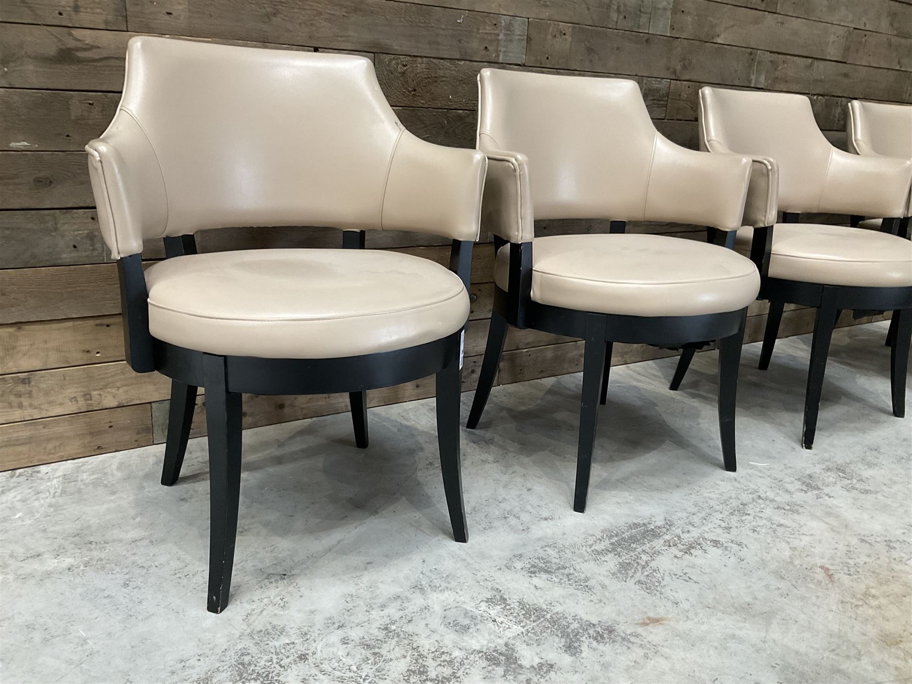 Four ebonised framed tub shaped armchairs, upholstered in beige fabric