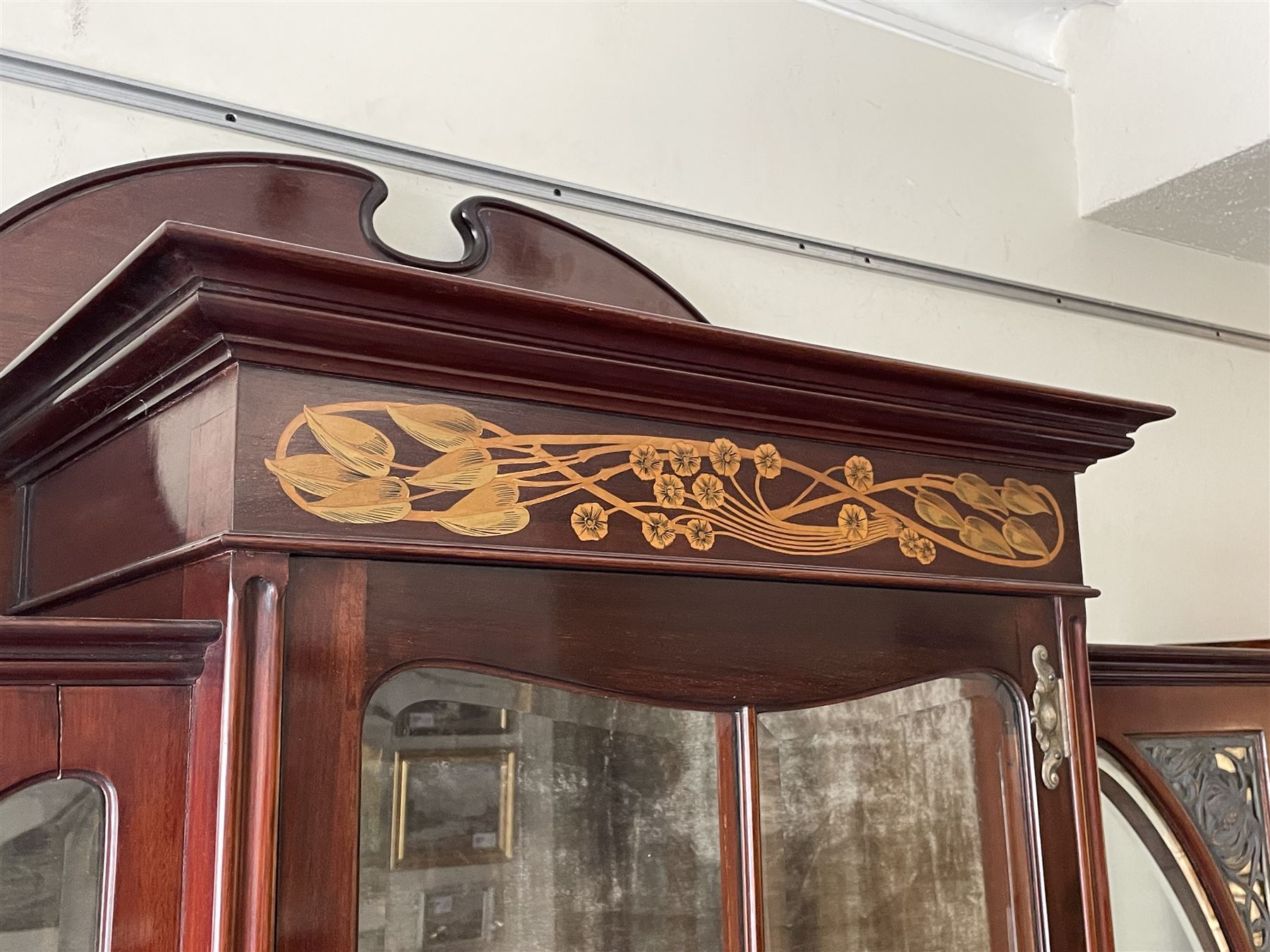 Art Nouveau period inlaid mahogany display cabinet, raised shaped and moulded pediment over projecting moulded cornices, the upper frieze inlaid with trailing branches and tulips, single astragal and bevel glazed door enclosed velvet lined interior fitted with shelves, flanked by curved glass panes decorated with pierced metal foliate spandrels, lower flanking shelves with mirror backs enclosed within shaped and pierced rails inlaid with flower heads, on tapering octagonal supports terminating to compressed pad feet, the lock stamped 'Salmon Bros, London' 