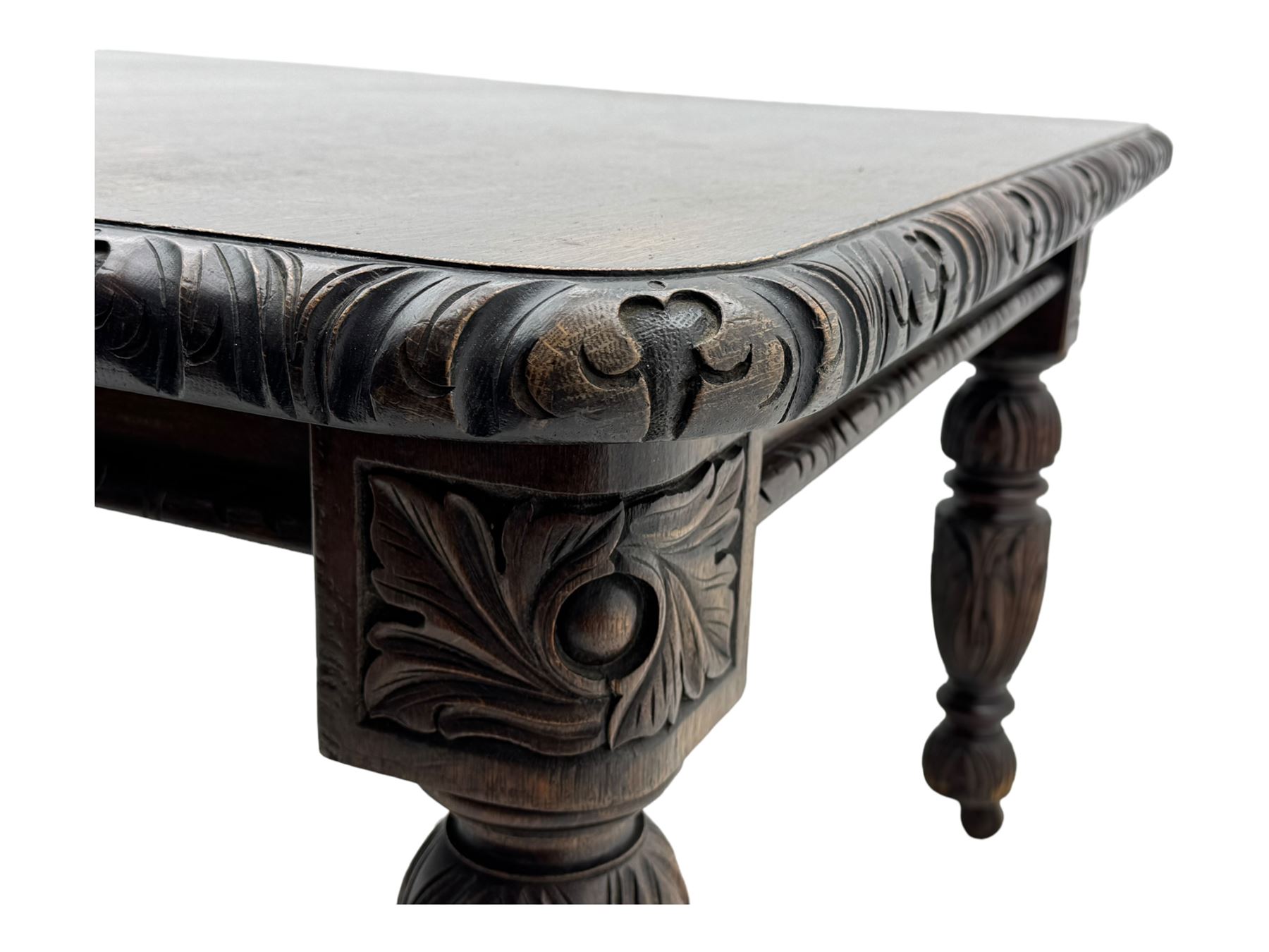 19th century heavily carved oak extending dining table, rectangular top with rounded corners and carved gadrooned edge, extending via winding mechanism with two additional leaves, raised on acanthus leaf-carved baluster supports terminating in ceramic castors