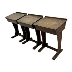 Three pitch pine school desks, each with rectangular lift-top with recessed ink well enclosing storage compartment, on trestle supports joined by stretcher