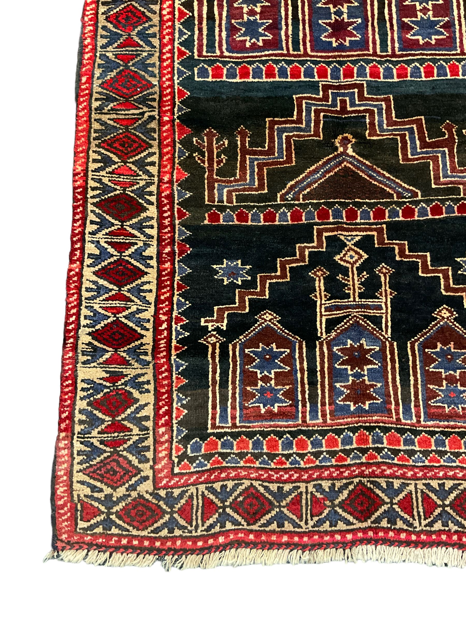 Baluchi dark indigo and crimson ground rug, decorated with cityscape within geometric border 