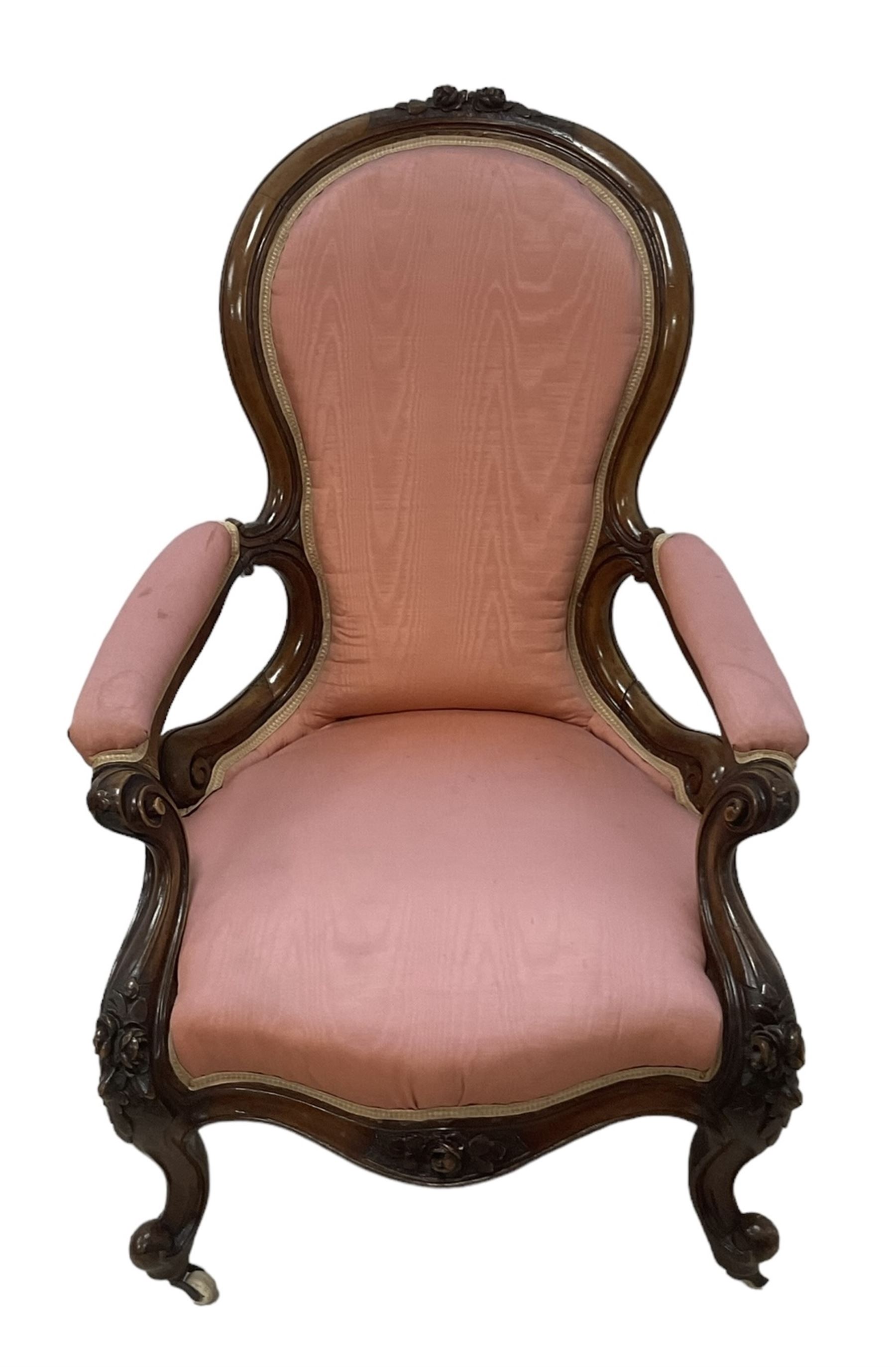 Victorian mahogany framed open armchair, spoon-back and sprung seat upholstered in pink fabric, scrolled arm terminals over serpentine fronted seat decorated with moulded carved floral motifs, cabriole supports with ceramic castors