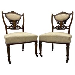 Pair of Edwardian inlaid rosewood bedroom chairs, the shaped cresting rail inlaid with extending floral decoration, upholstered back over pierced and scroll carved splat decorated with further floral inlays, upholstered sprung seats, on square front supports with shaped peg feet