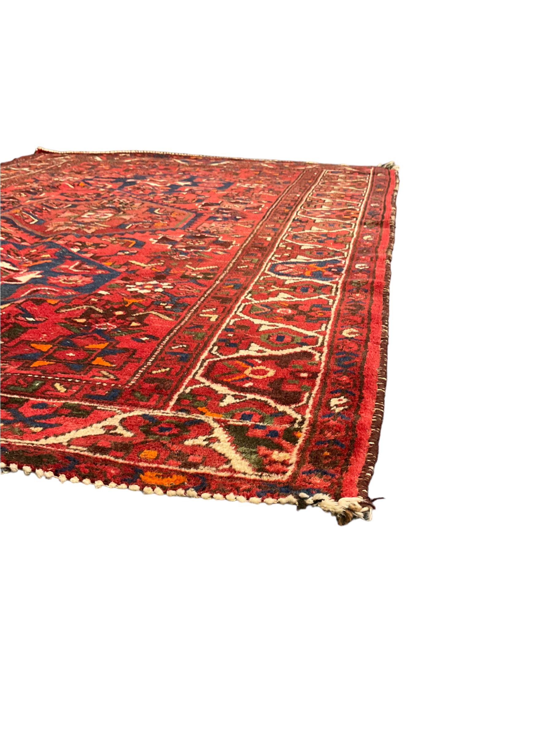 Persian Hamadan rug, red ground with overall geometric design, the field with three extended lozenges, decorated with geometric and stylised flower head motifs, the border and guards decorated with repeating geometric motifs