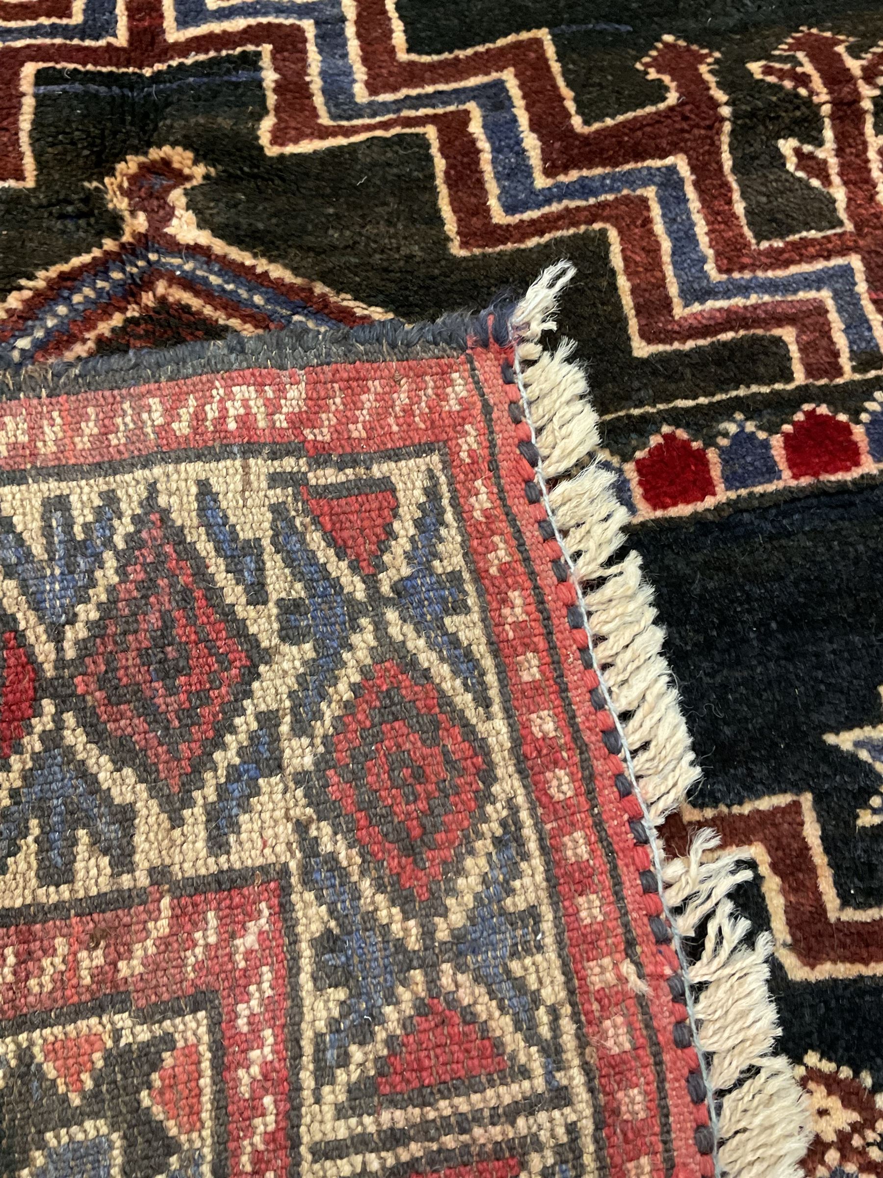 Baluchi dark indigo and crimson ground rug, decorated with cityscape within geometric border 