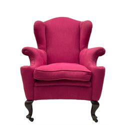 Georgian design hardwood-framed wingback armchair, arched cresting rail over curved wingback, rolled arms on scrolled cushioned supports, reverse bow-front, upholstered in claret red fabric with loose seat cushion, on cabriole front feet and brass castors 