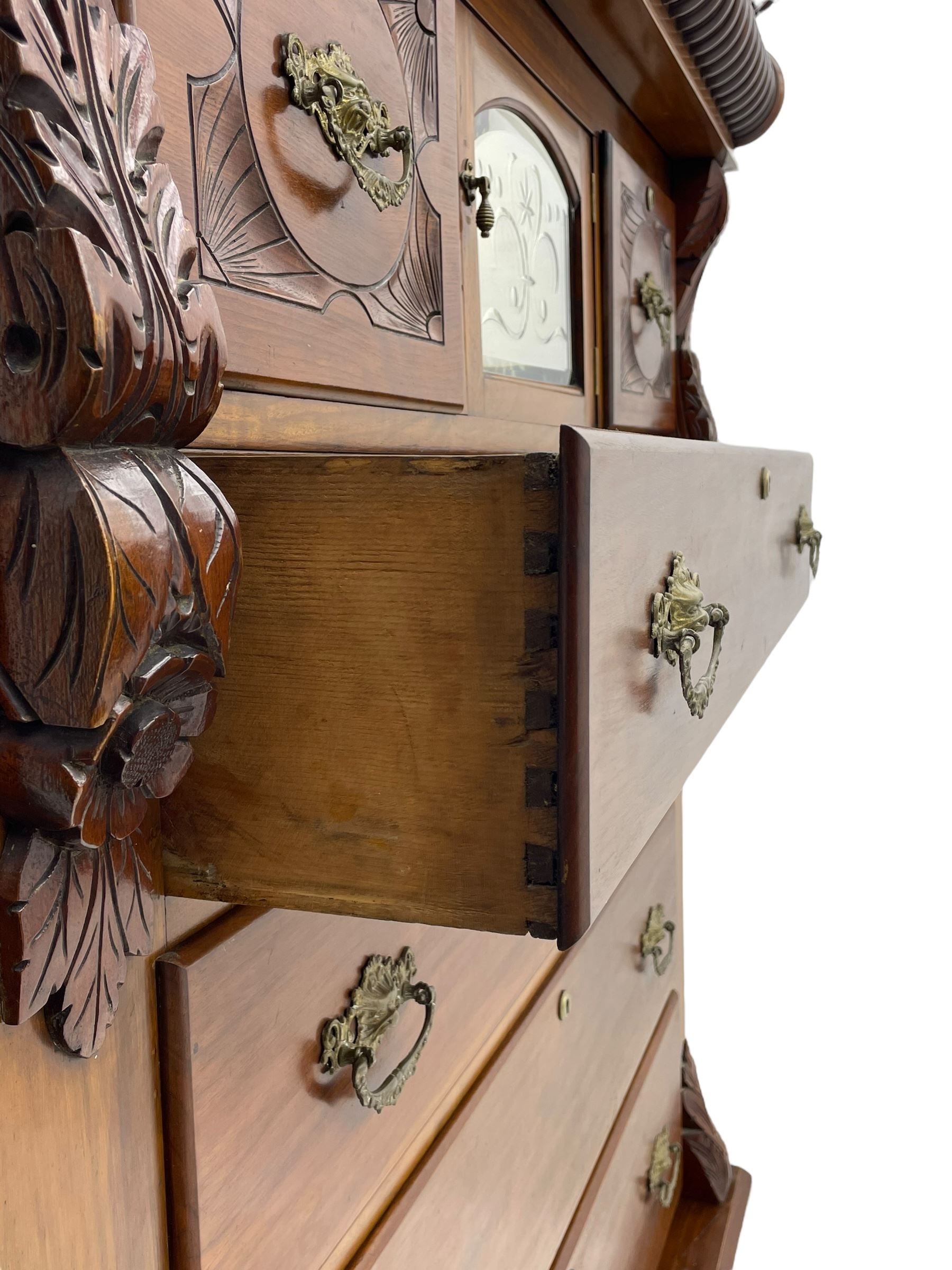 Late Victorian walnut Scotch chest, projecting cornice with turned quarter column mounts over matching half column to frieze, fitted with two upper short drawers with central cupboard, bevelled mirror glazed cupboard door, four graduating drawers below, foliage and flower head carved brackets to the uprights, panelled sides, chamfered plinth on turned feet