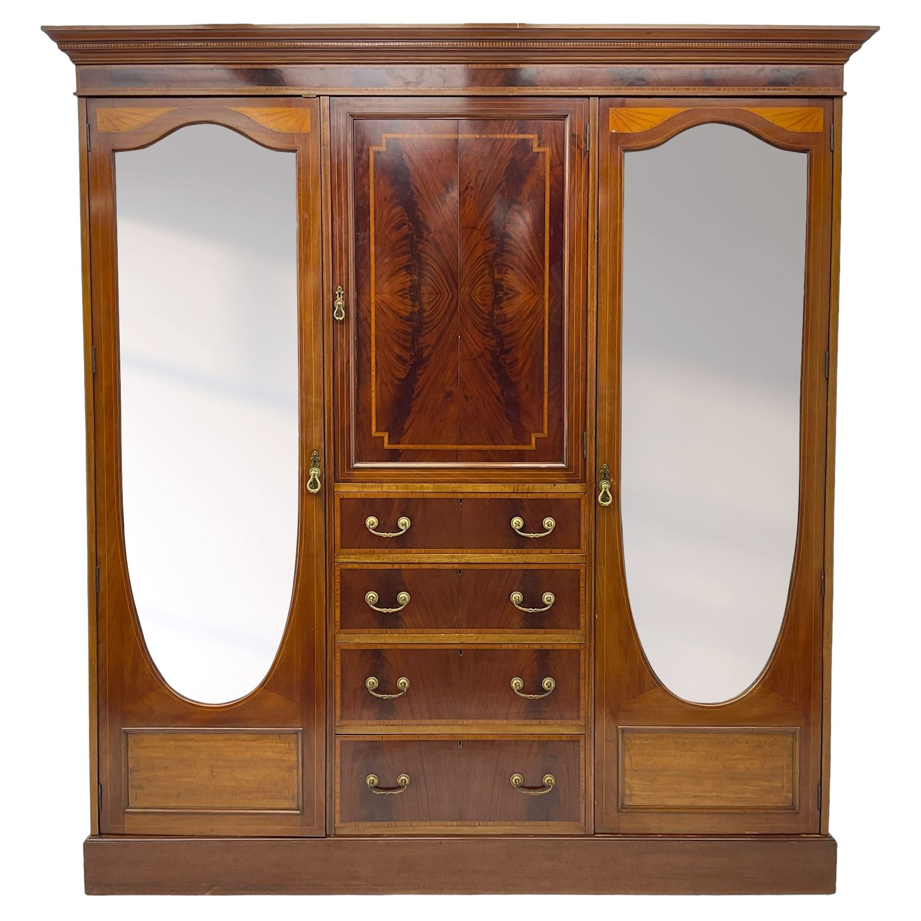 Edwardian inlaid mahogany combination wardrobe, projecting moulded cornice over figured frieze with satinwood banding, the central section fitted with cupboard over four long drawers, figured matched veneers and satinwood bands, flanked by two full height compartments enclosed by bevelled shield shaped mirror doors, satinwood fan inlaid spandrels, on moulded skirt base 