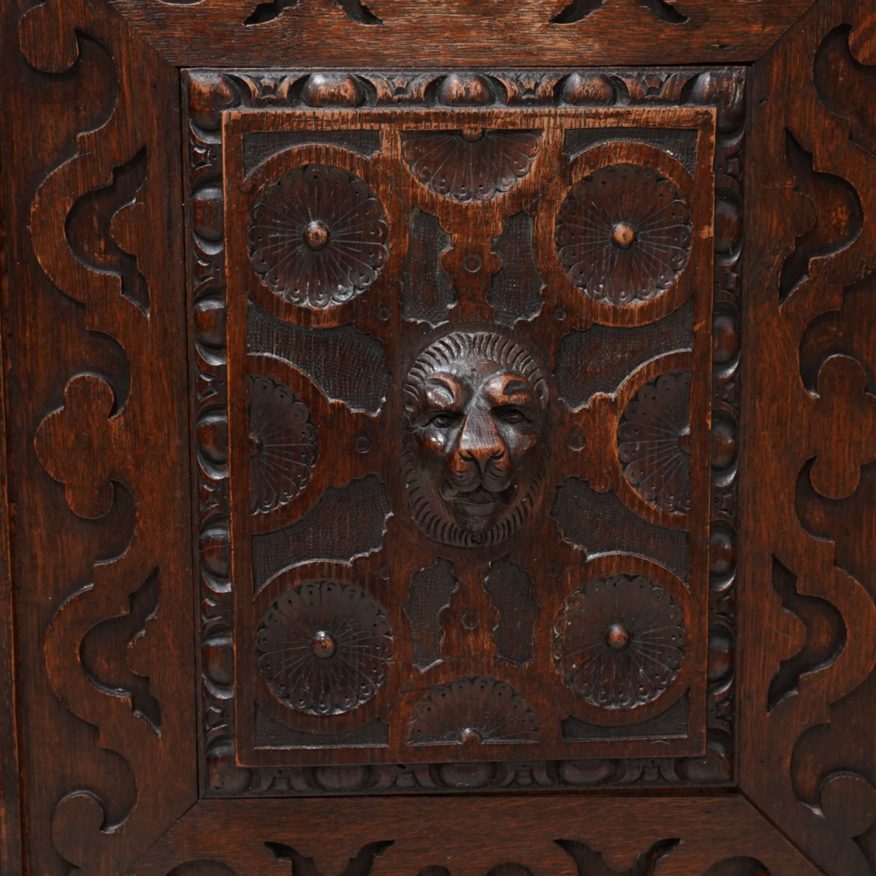 19th century Jacobean Revival heavily carved oak side cabinet, rectangular top with moulded edge, the frieze drawer applied with a central green man carved handle and surrounded scrolled acanthus leaves, over two panelled cupboards with egg-and-dart and rosette motifs with central lion mask mounts, flanked by uprights with further lion masks over protruding fruit and floral vines, lower moulded edge on square feet