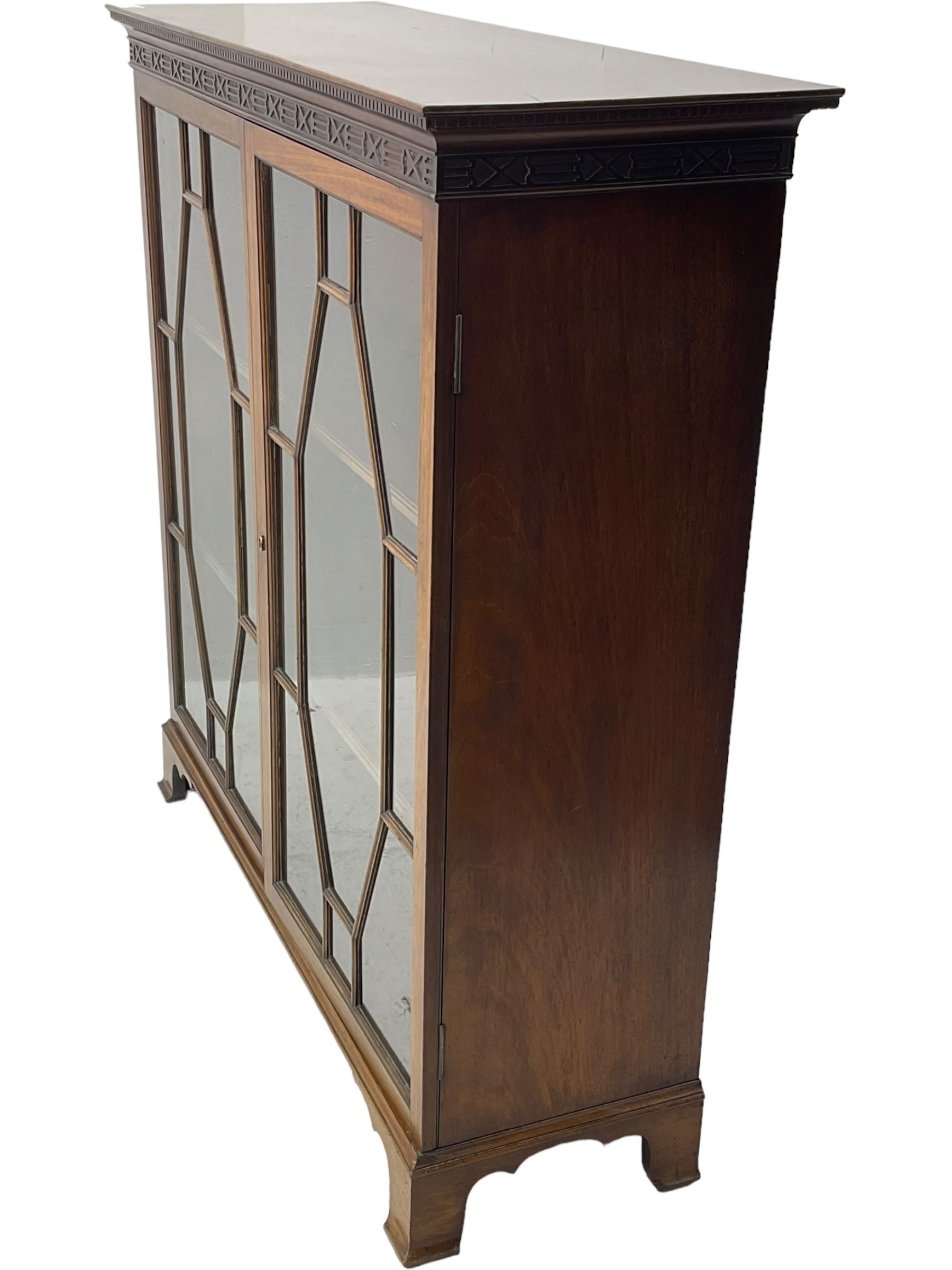 Early 20th century mahogany bookcase, projecting dentil cornice over blind fretwork frieze, enclosed by two astragal glazed doors, on shaped bracket feet 