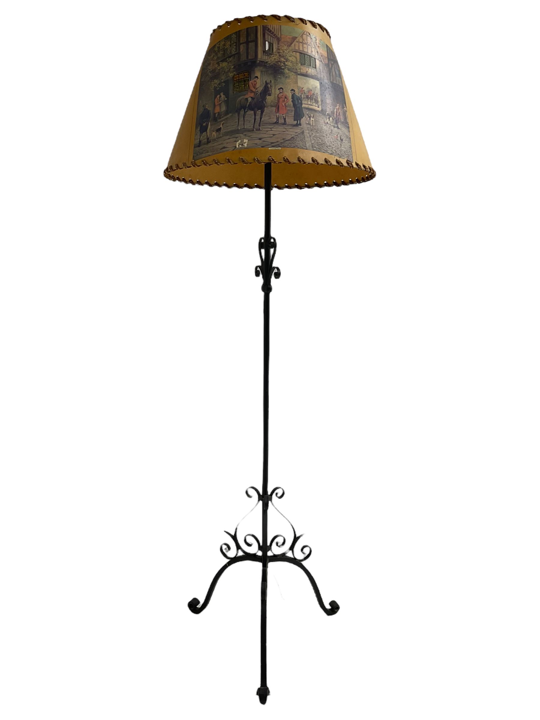 20th century wrought metal standard lamp, decorated with scrolls and on tripod base, with conical shade depicting hunting scene (H172cm); and a wrought metal wall hanging flower pot holder (W92cm)