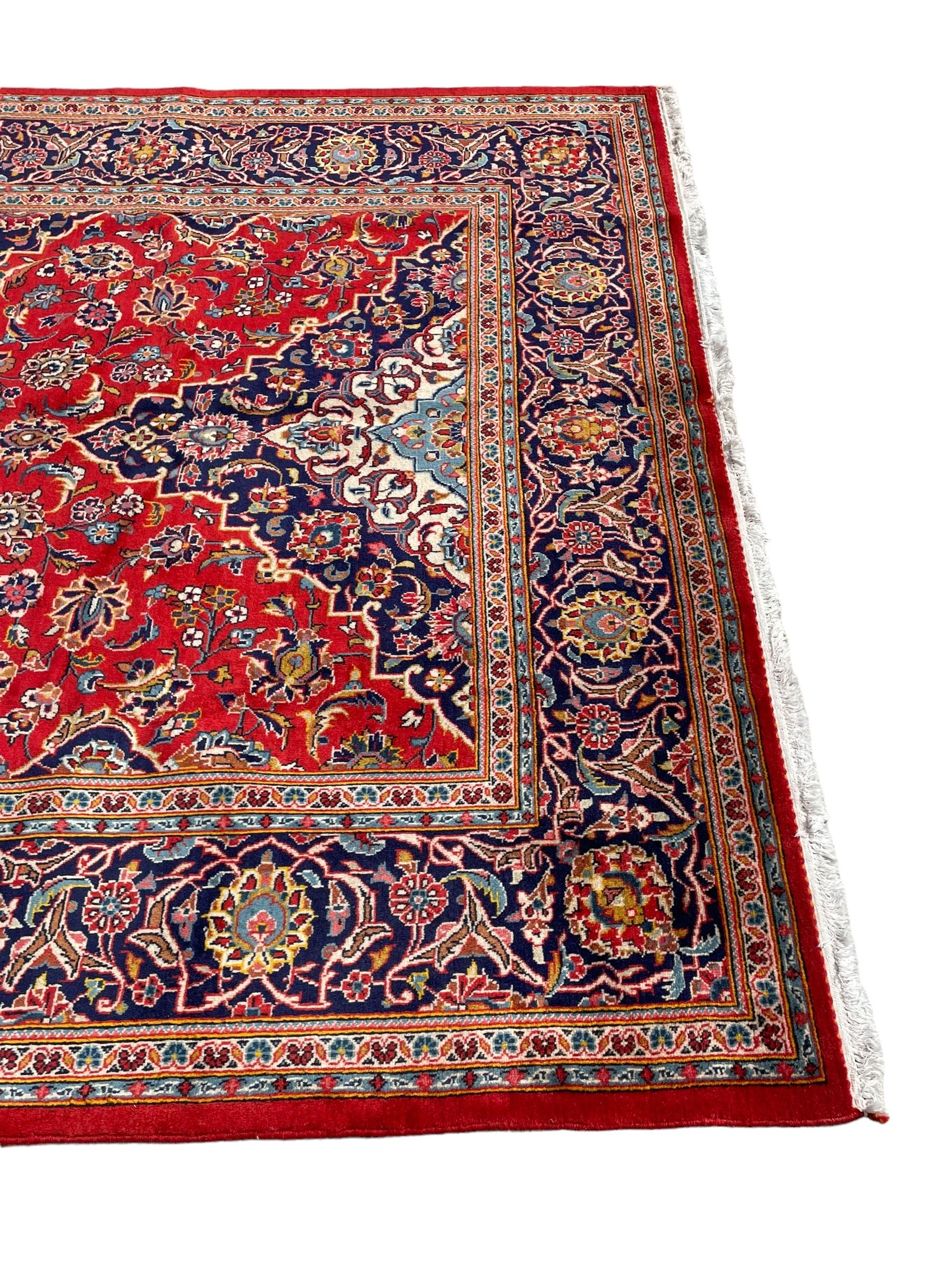 Persian Kashan crimson ground rug, overall arabesque design, the field decorated with swirled leafy branches and palmettes, indigo ground border decorated with repeating pattern, within guard stripes 