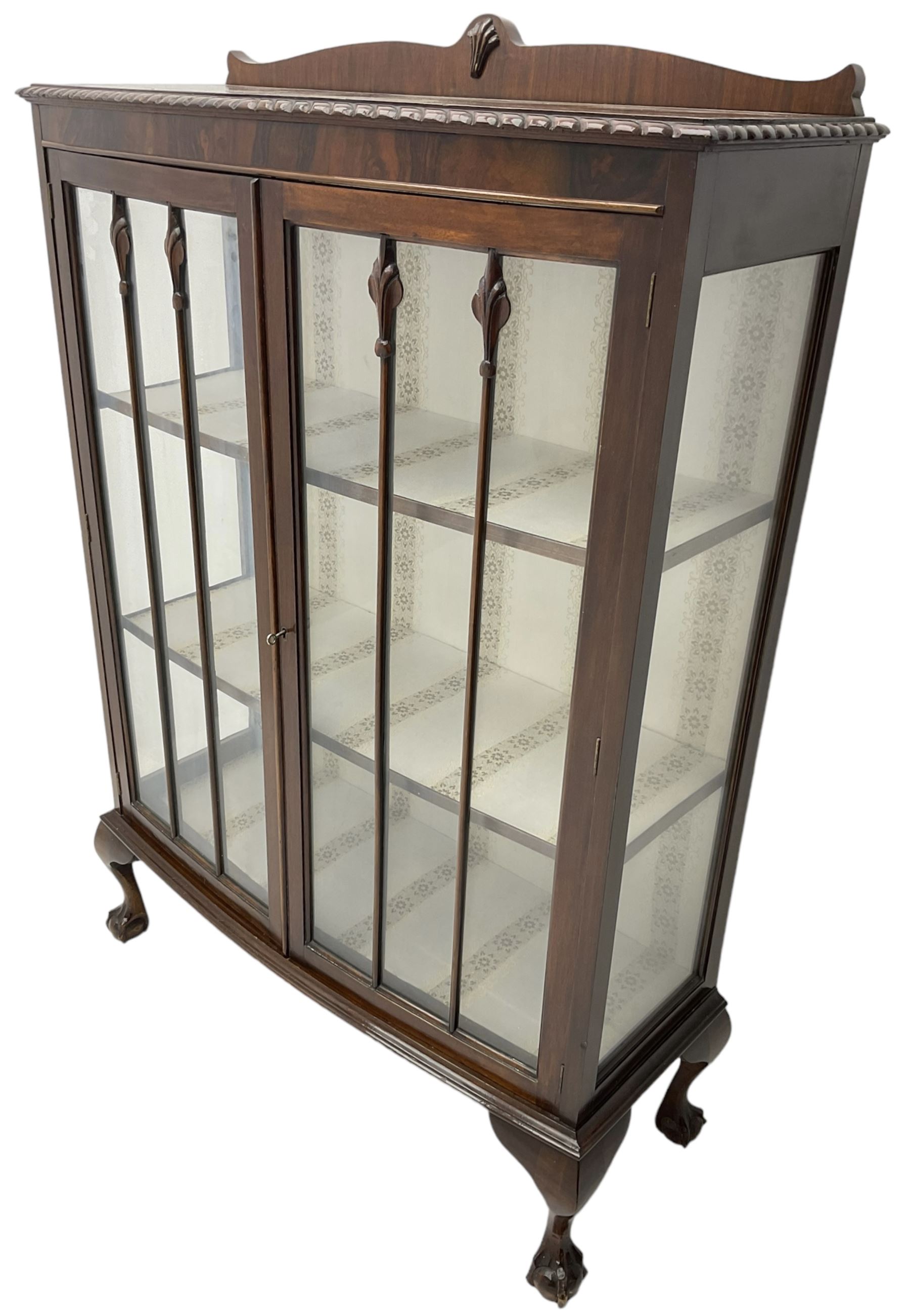 Early 20th century figured walnut bow-front display cabinet, enclosed by two glazed doors, on ball and claw cabriole feet